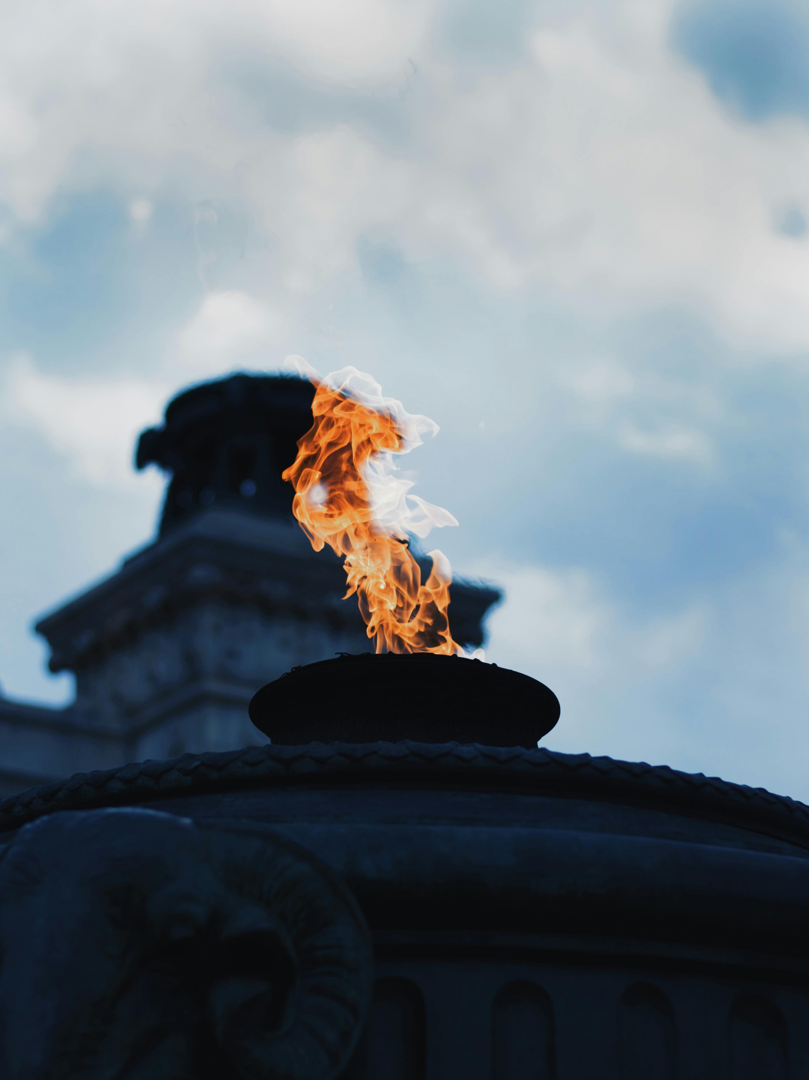 Gratis En dramatisk evig flamme på et monument mot en overskyet himmel, som symboliserer minne. Arkivbilde