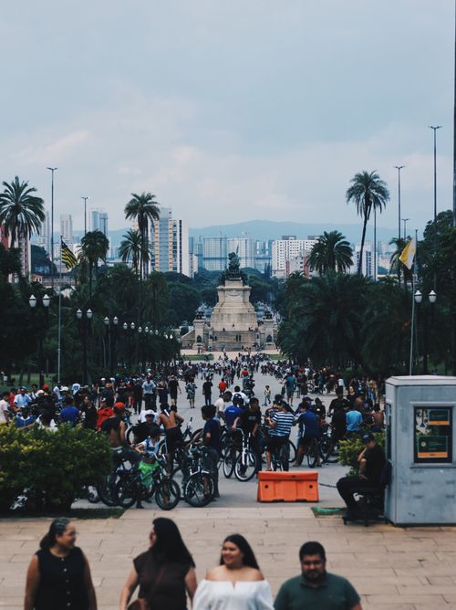 Free A busy park with a crowd of people and cyclists, framed by palm trees and city skyline in the background. Stock Photo