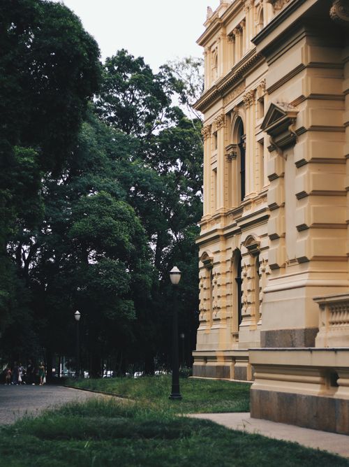 Free Historic building with classical architecture surrounded by lush greenery in a serene park setting. Stock Photo