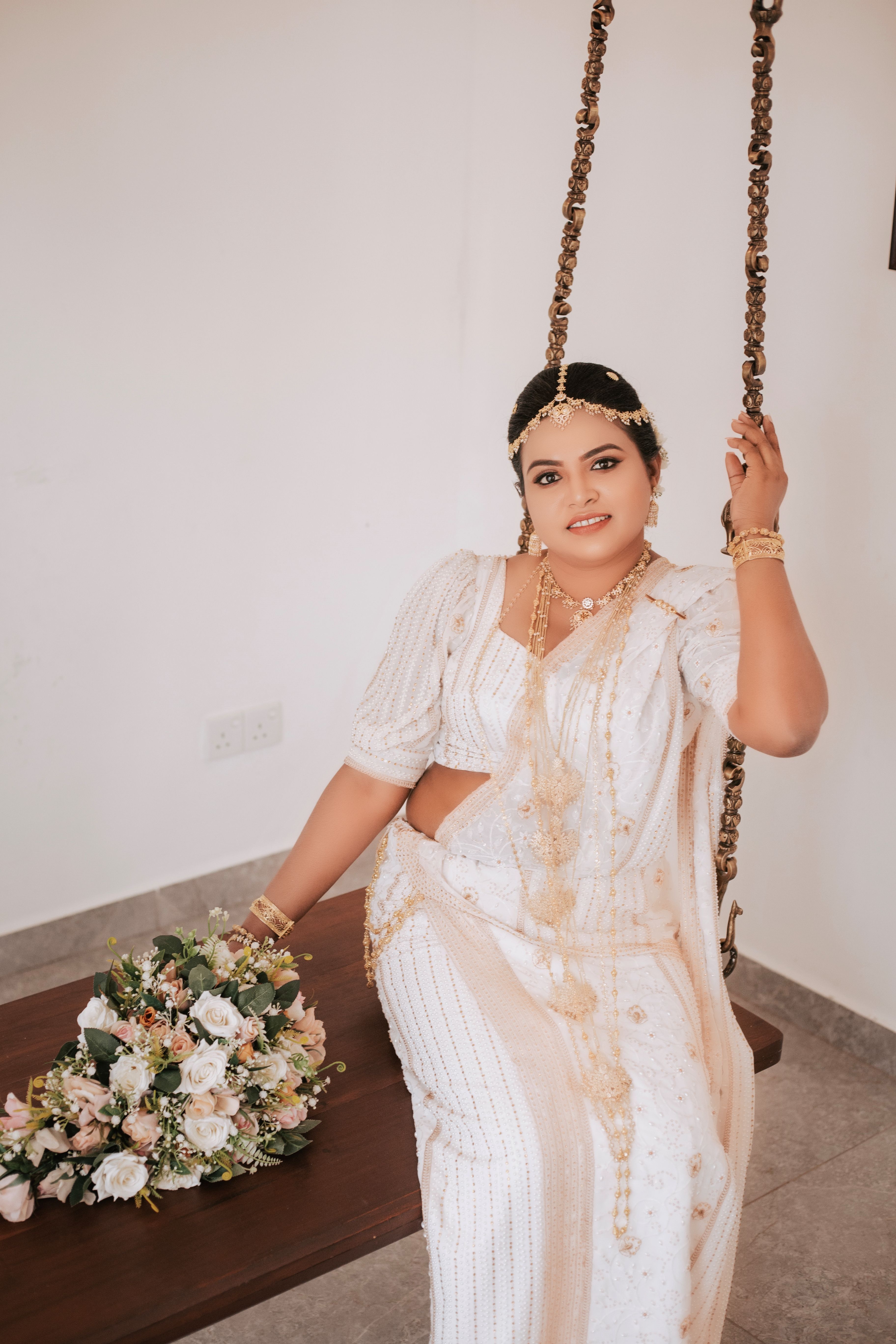 Kandyan bride in white osariya seated on a wooden swing