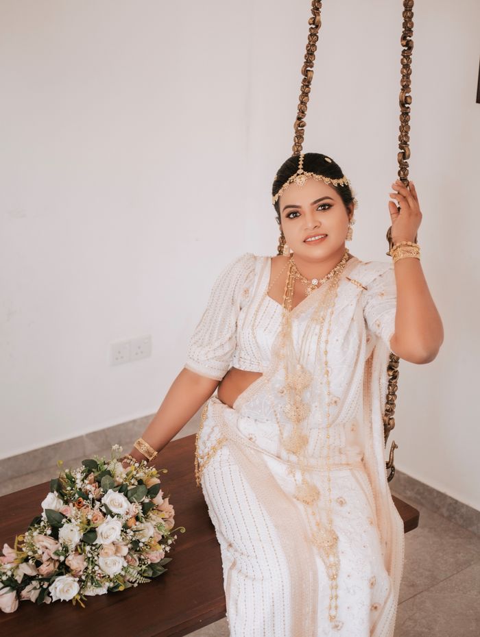 Kandyan bride in white osariya seated on a wooden swing