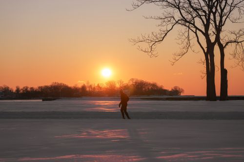 Free A person walking through a snowy landscape at sunset with trees and orange sky. Stock Photo