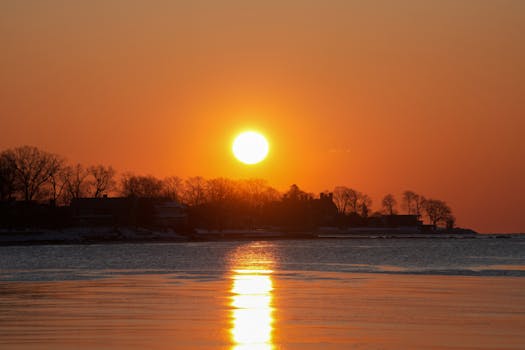 A breathtaking sunset over a calm lake with silhouetted trees on the horizon, showcasing vivid orange hues.