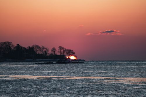 Free Peaceful sunset over the sea with silhouetted trees and vibrant sky colors. Stock Photo