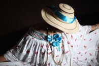 A close-up of a traditional pollera dress adorned with a straw hat and vibrant blue ribbon, showcasing cultural elegance.
