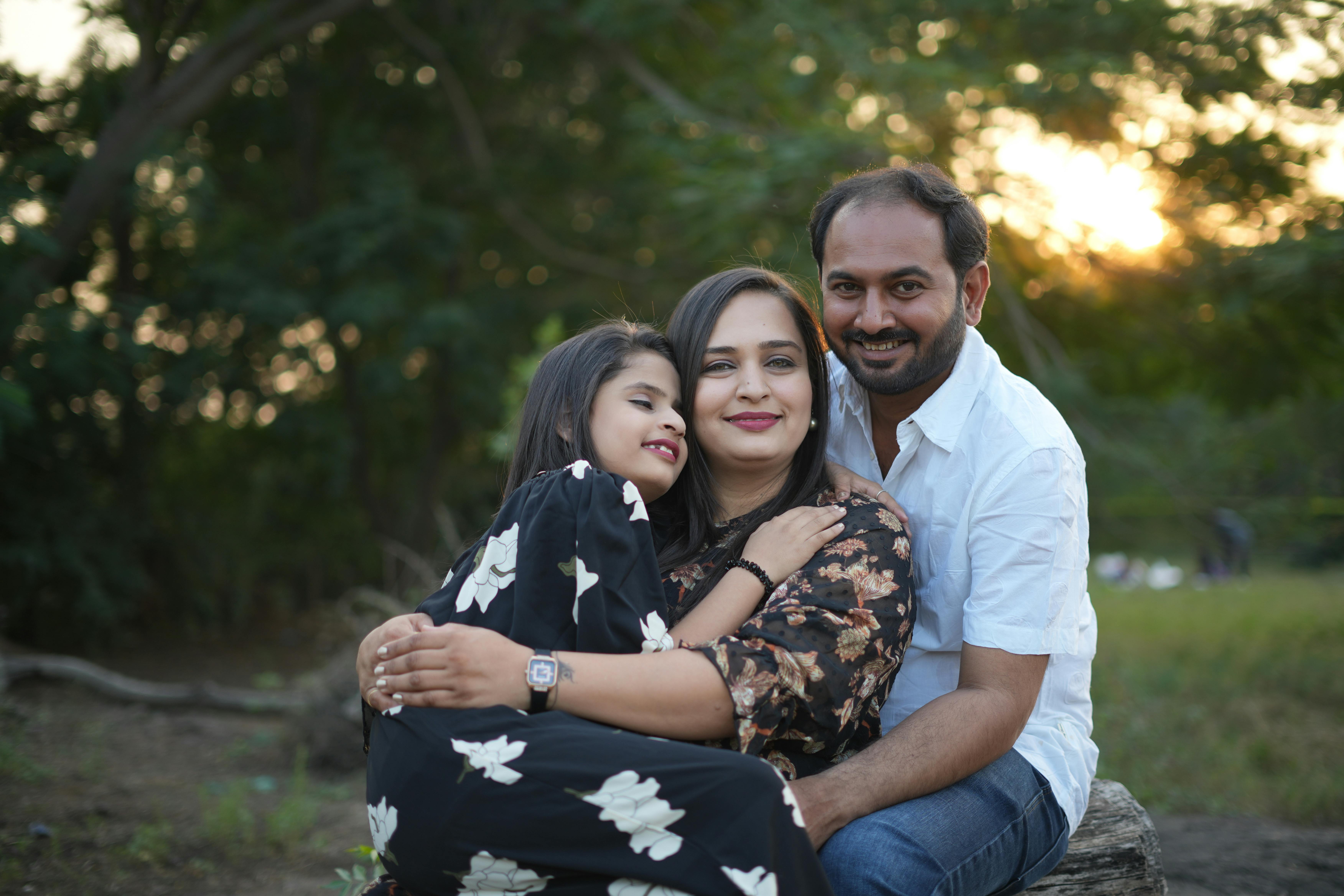 A happy family of three enjoying quality time together outdoors during sunset, embracing each other joyfully.