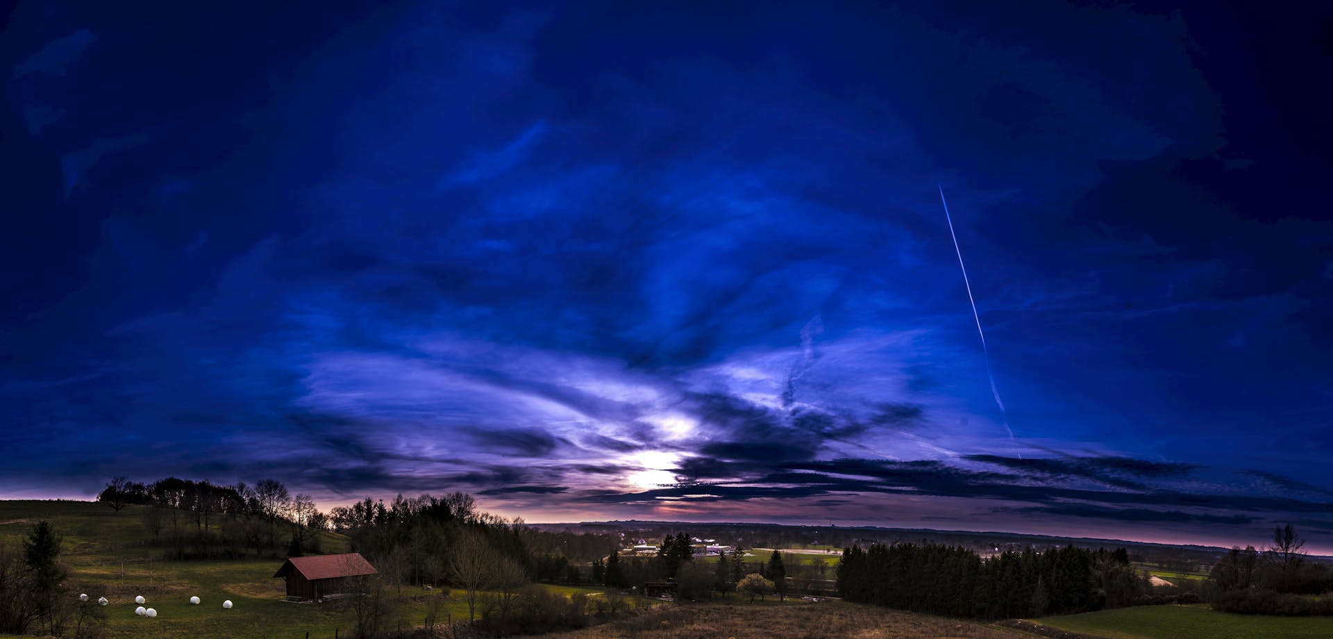 Captivating dusk sky over serene rural landscape with fields and trees.