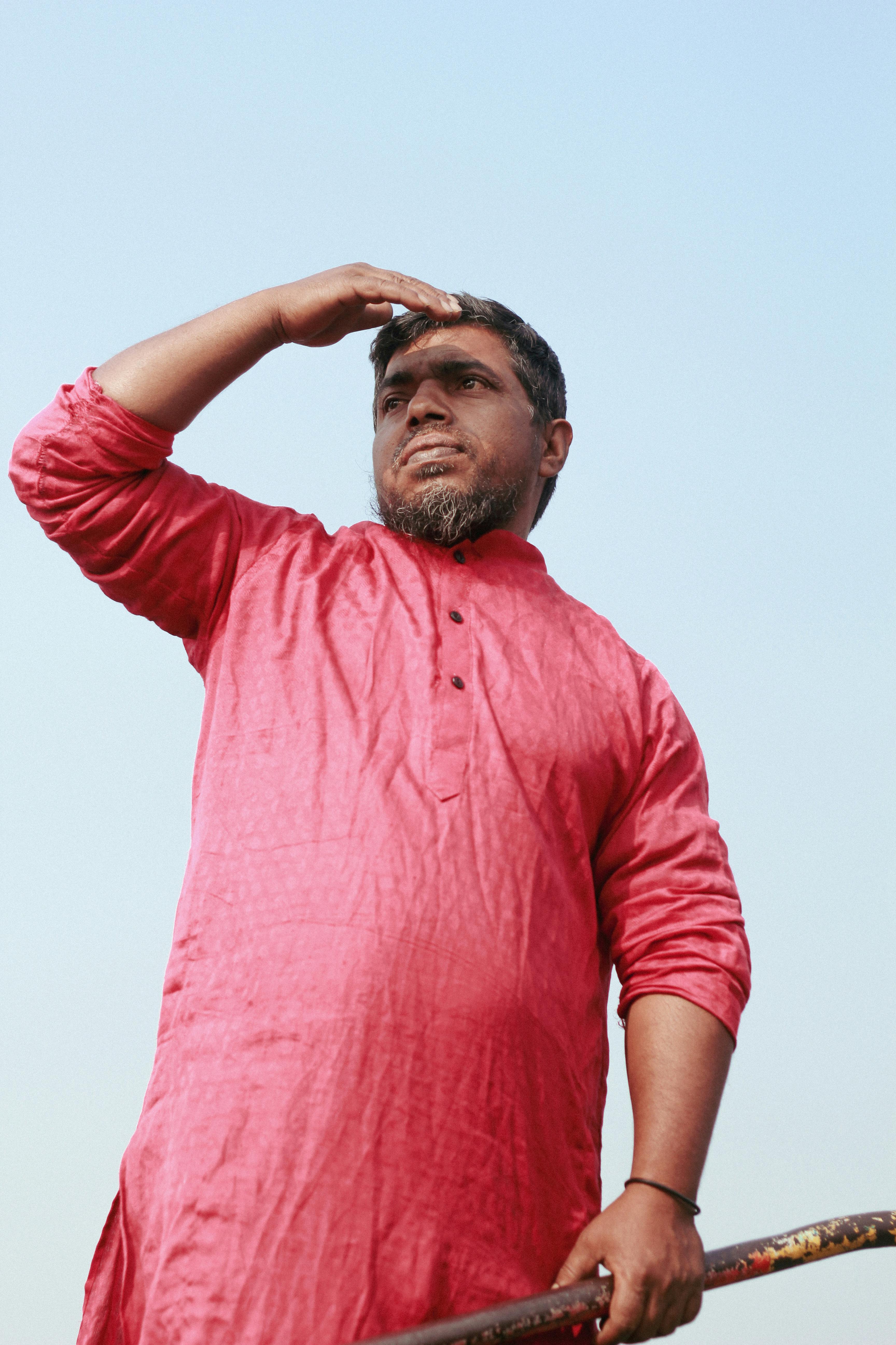 Man in a red kurta looking into the distance over water in Dhaka, Bangladesh.