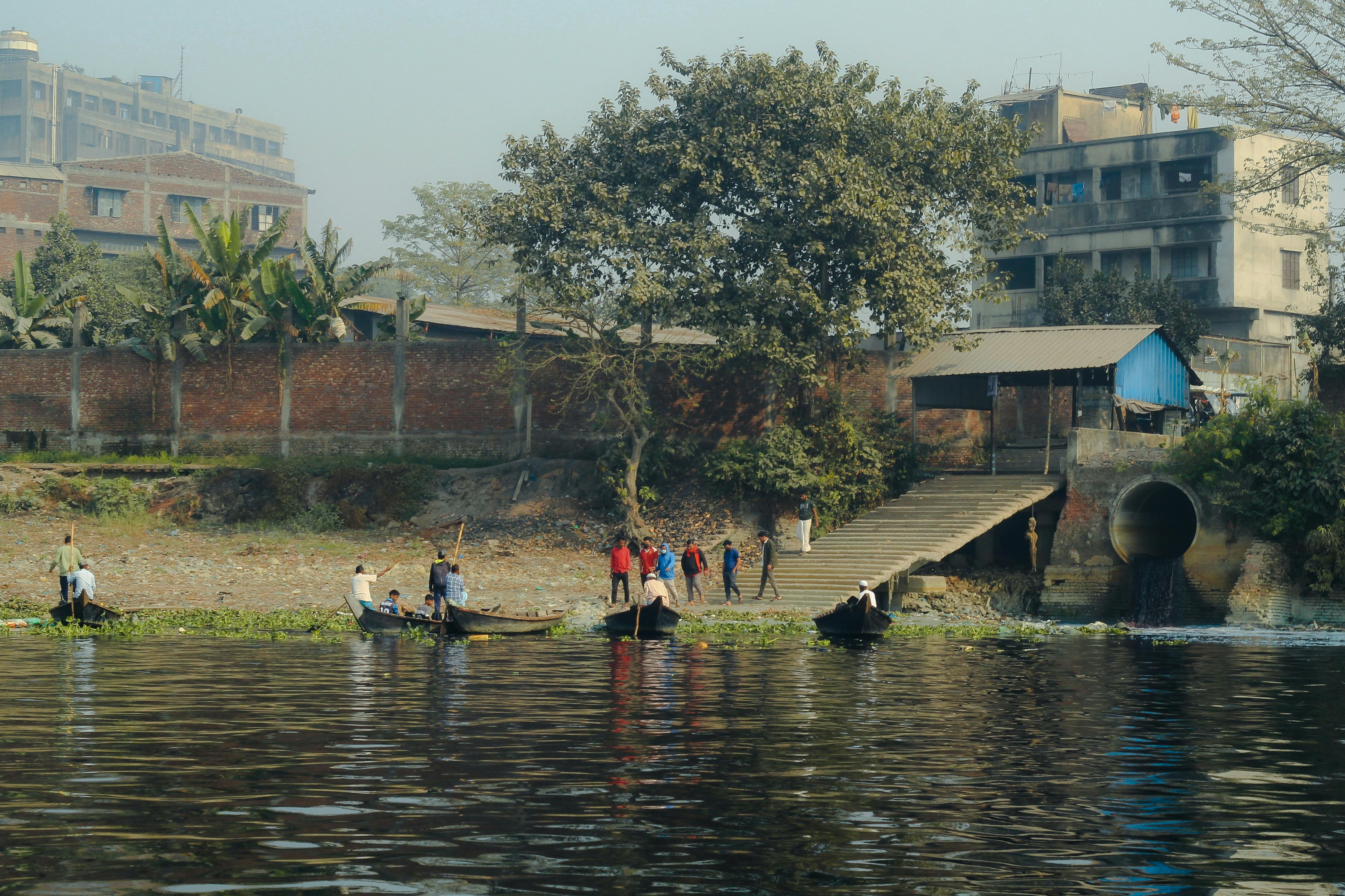Urban riverfront scene in Dhaka with people and boats, capturing vibrant daily life along the waterfront.