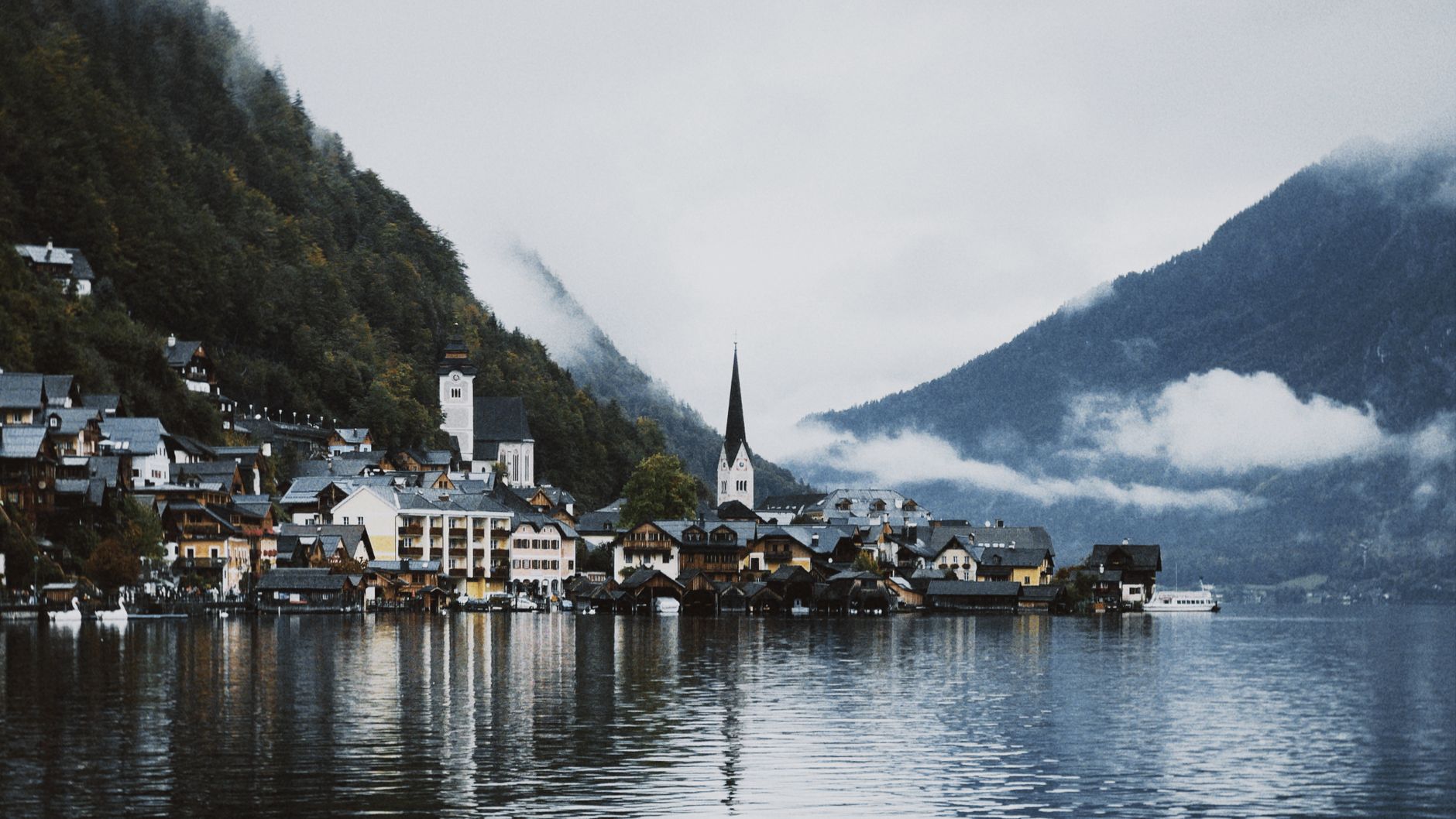 Scenic view of Hallstatt village surrounded by mountains and lake in misty atmosphere.