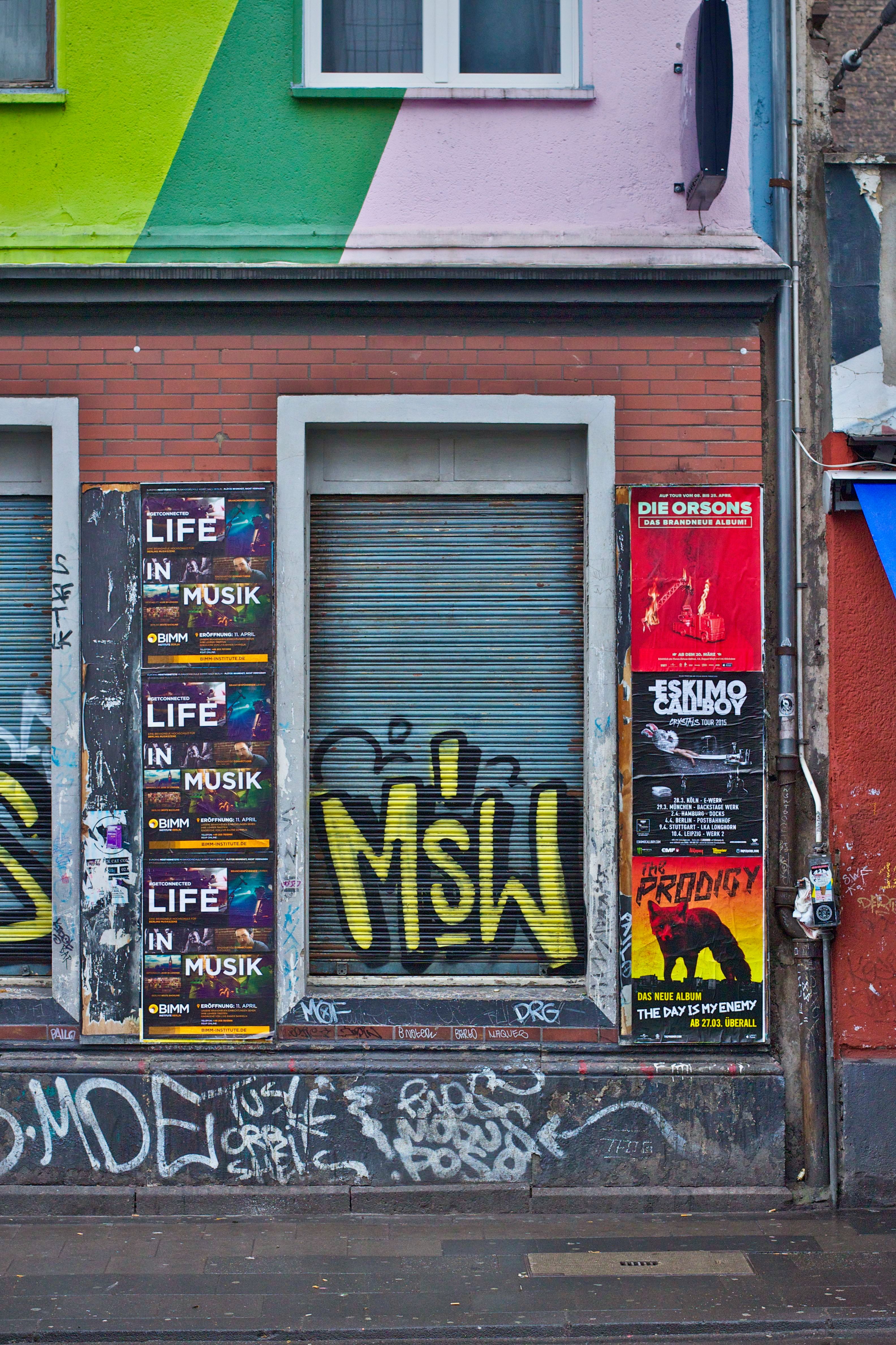 Colorful posters and graffiti on a street wall showcase urban art and upcoming music events.