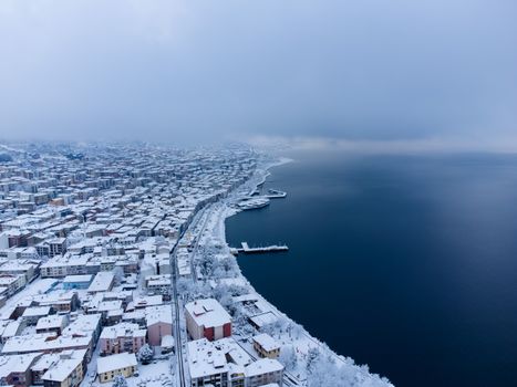 Stunning aerial view of a snow-covered coastal city in winter, overlooking a serene sea.