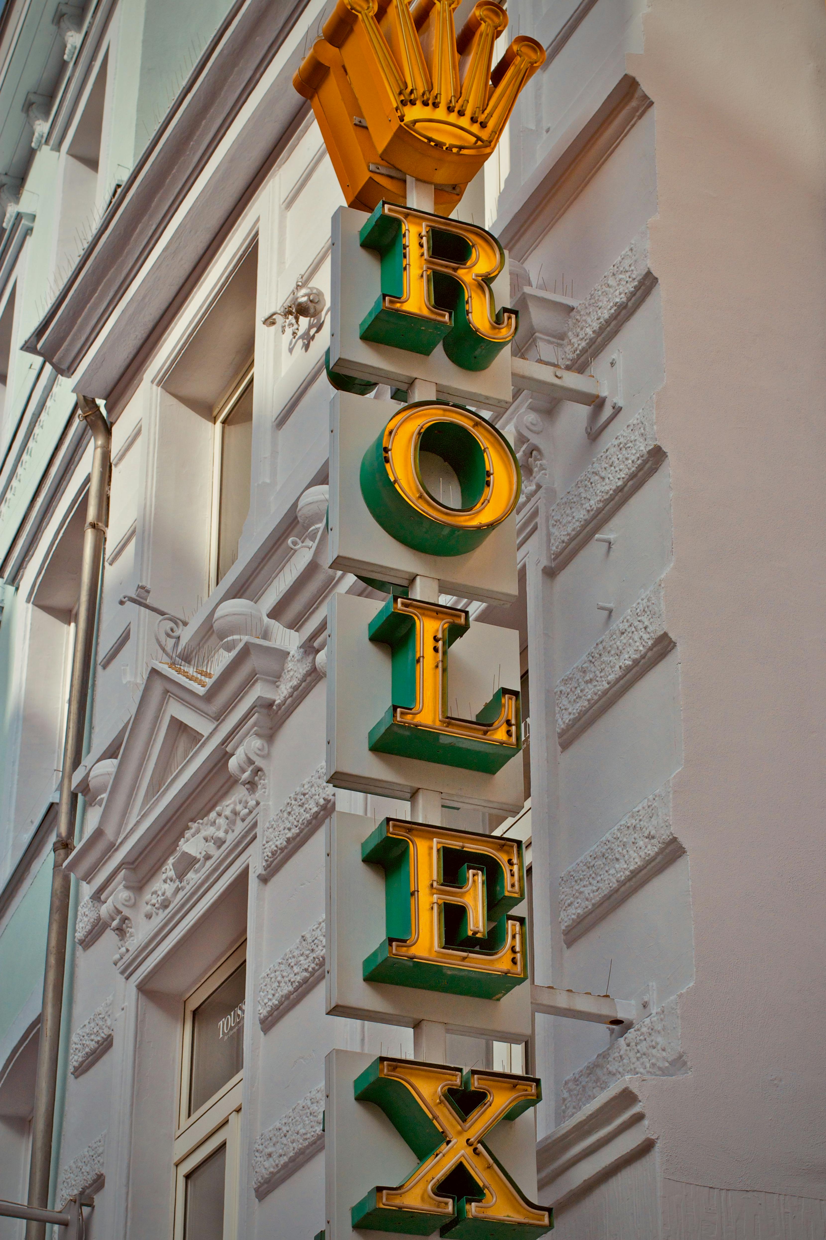Gratis Nærbilde av et vertikalt Rolex-skilt på en bygningsfasade med kongelig krone-logo. Arkivbilde