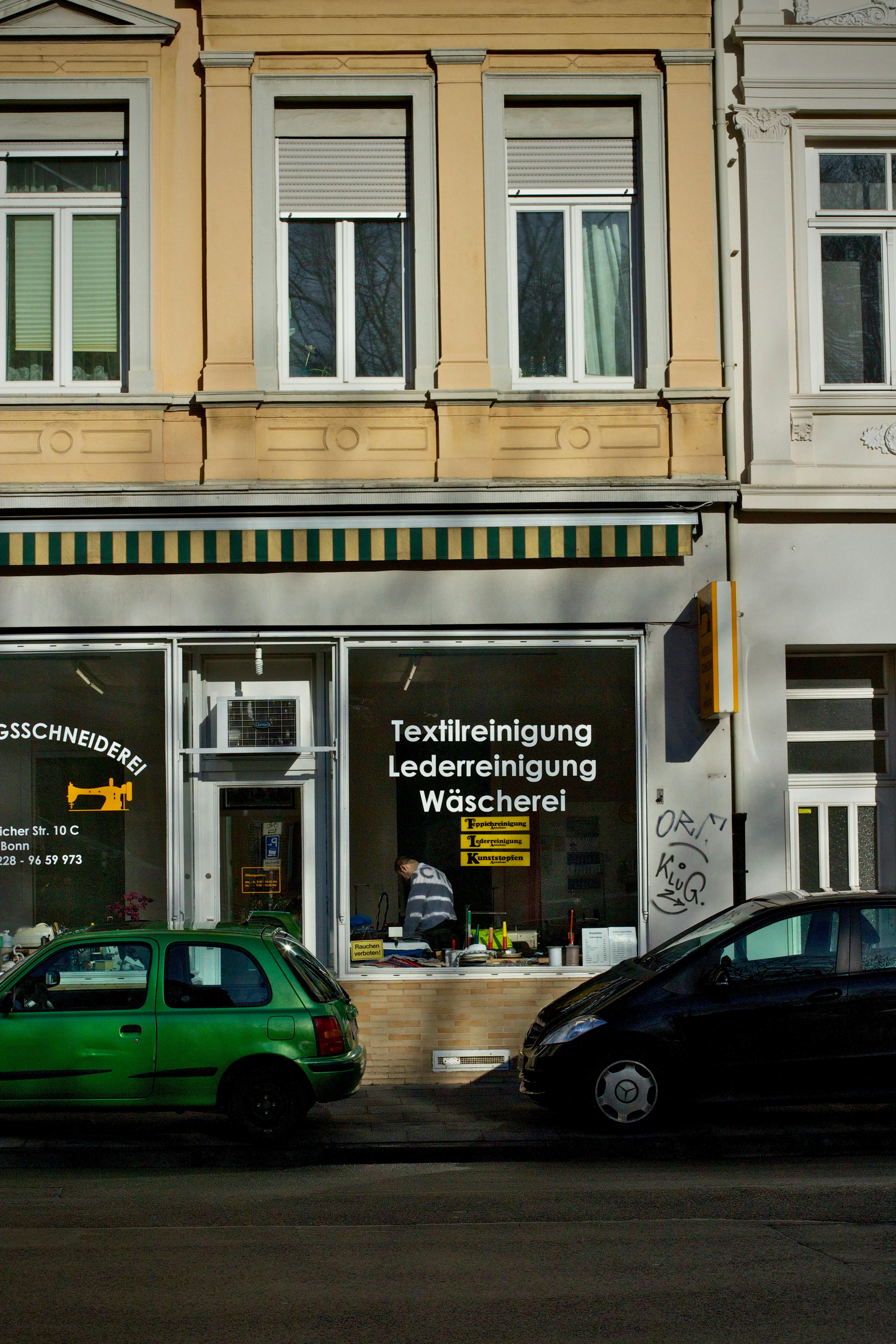 Exterior view of a German dry cleaning shop with parked cars and urban architecture.