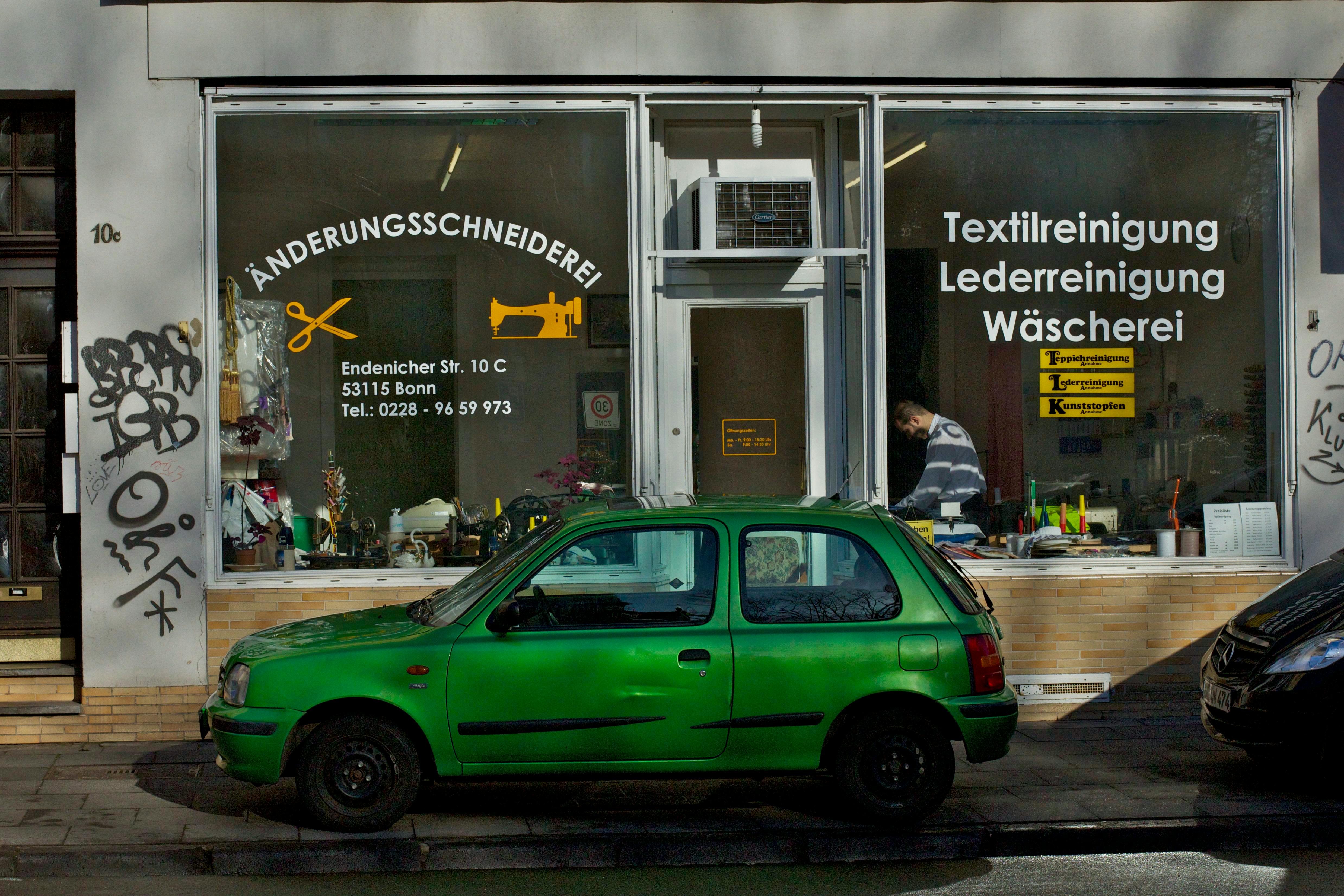 A green car parked outside a tailor shop in Bonn, Germany.
