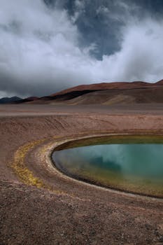 Dramatic view of a crater lake in a volcanic desert landscape under cloudy skies.