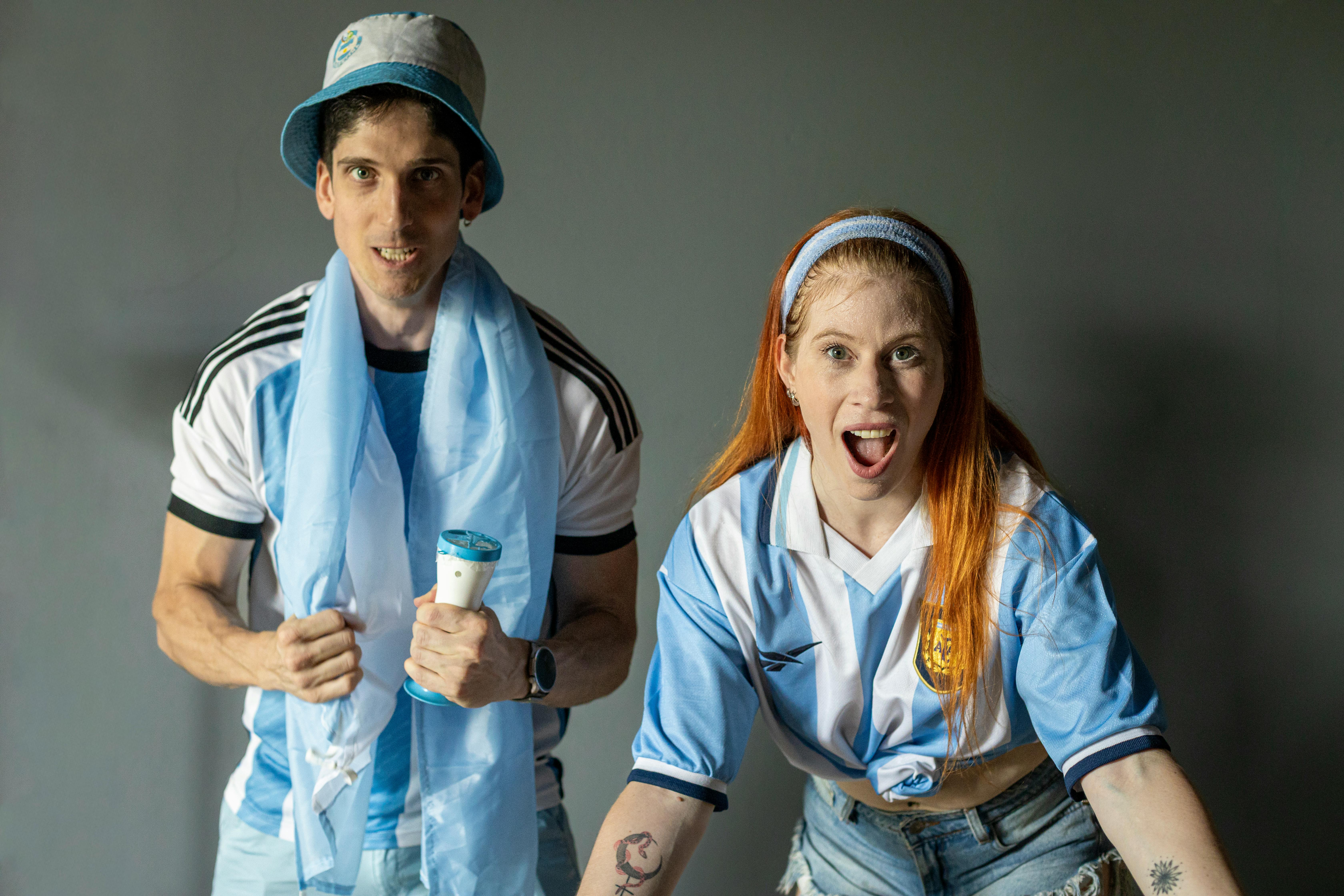 Two excited fans in Argentina jerseys express joy and support indoors.