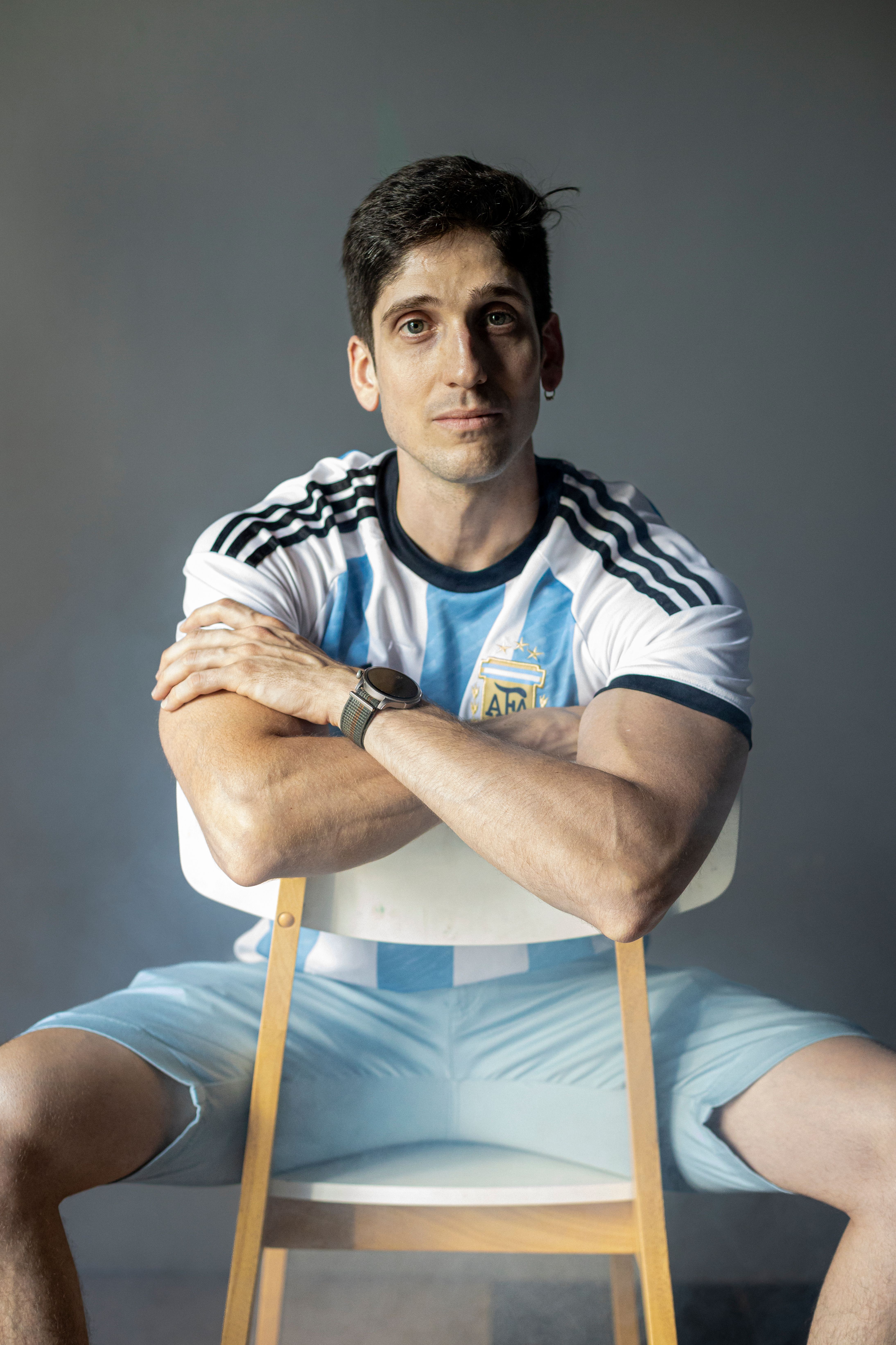 Portrait of a confident man in an Argentina football jersey sitting on a chair.