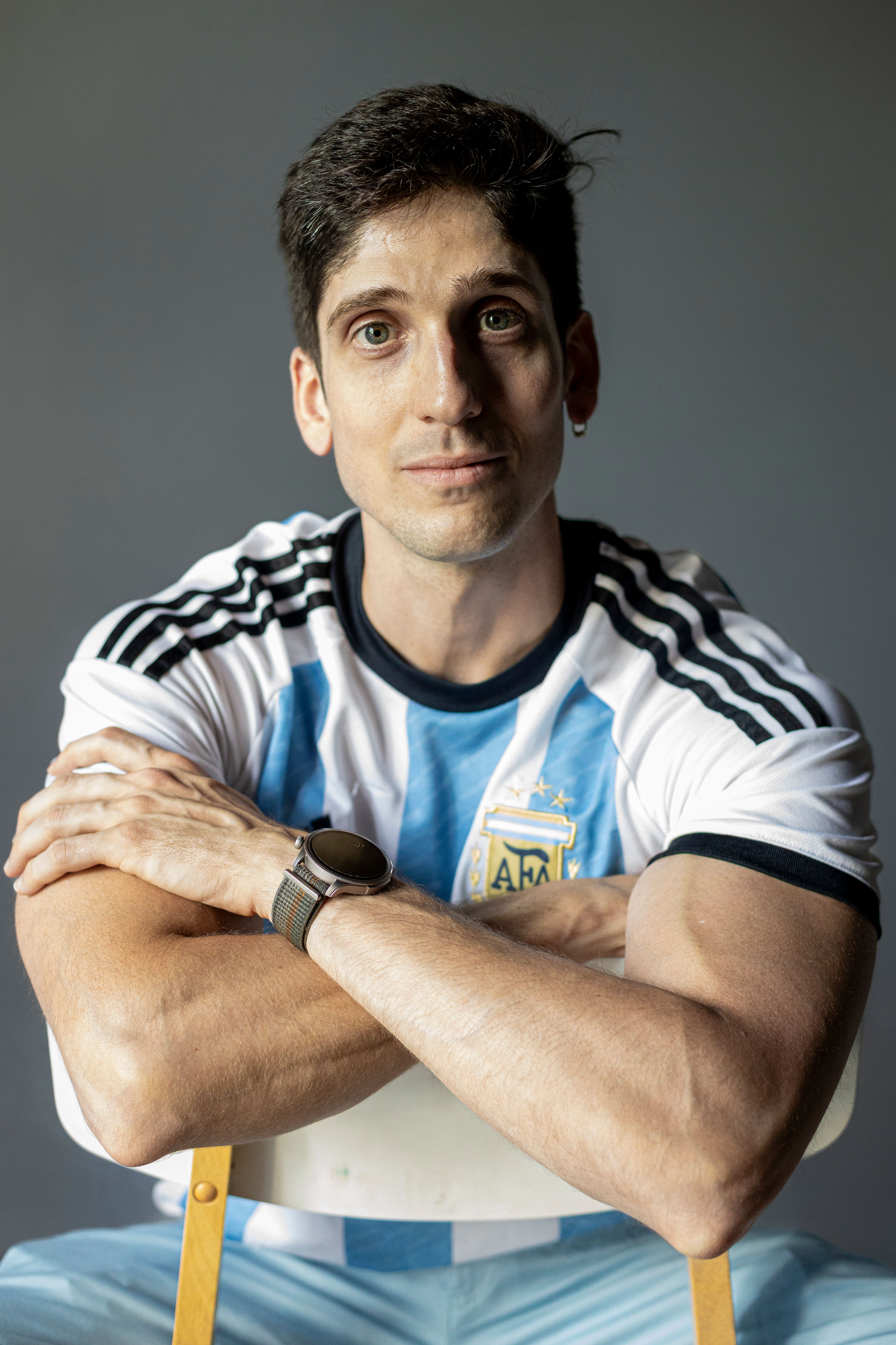 Confident man wearing Argentina soccer jersey sitting indoors, representing sports enthusiasm.