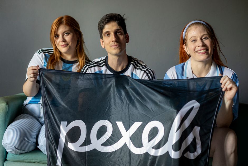 Three adults with an Argentina themed flag, smiling indoors.