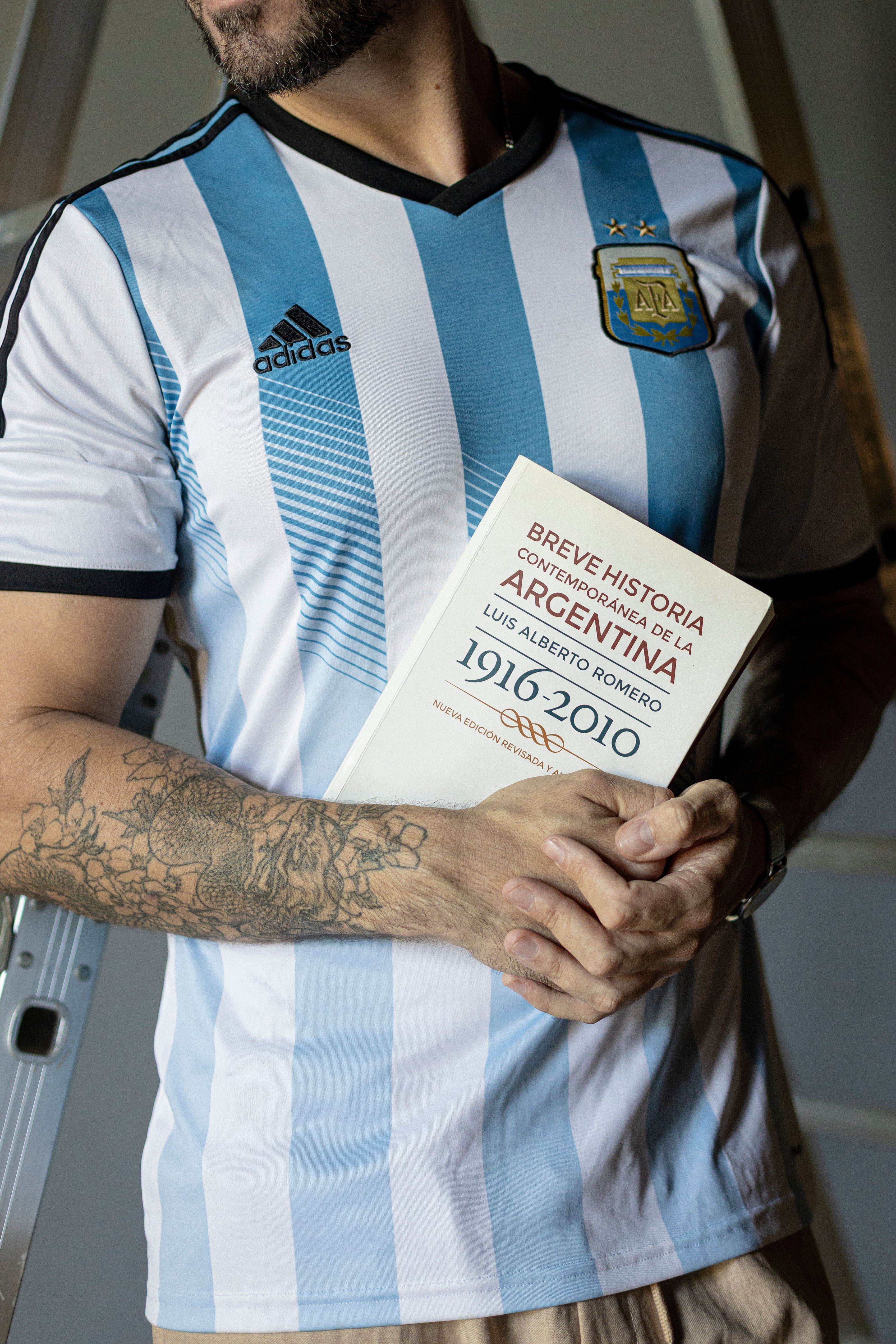 Person wearing Argentina jersey holding history book, showcasing national pride.