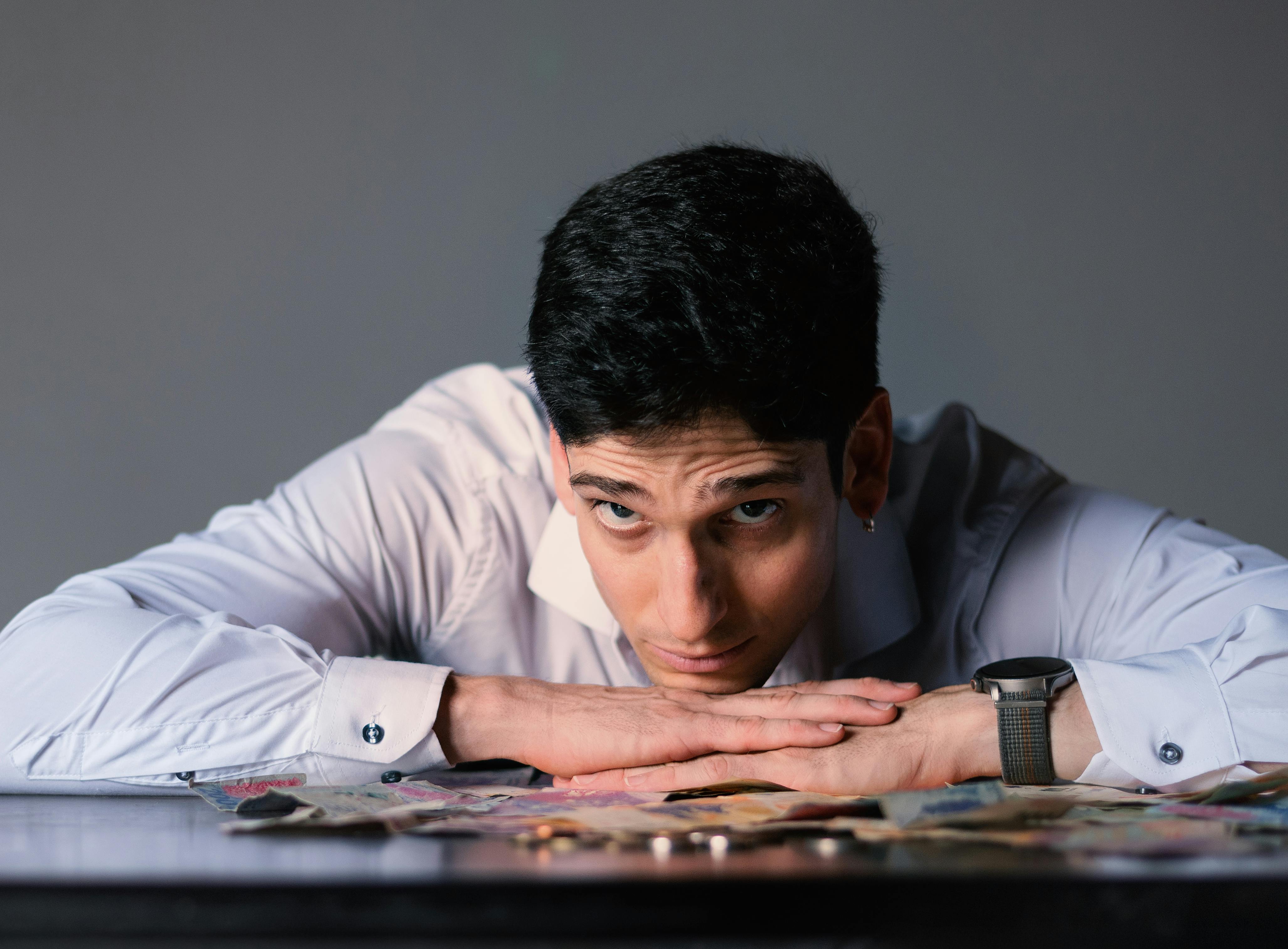 Portrait of a man in a white shirt leaning on a table covered with cash in Buenos Aires.