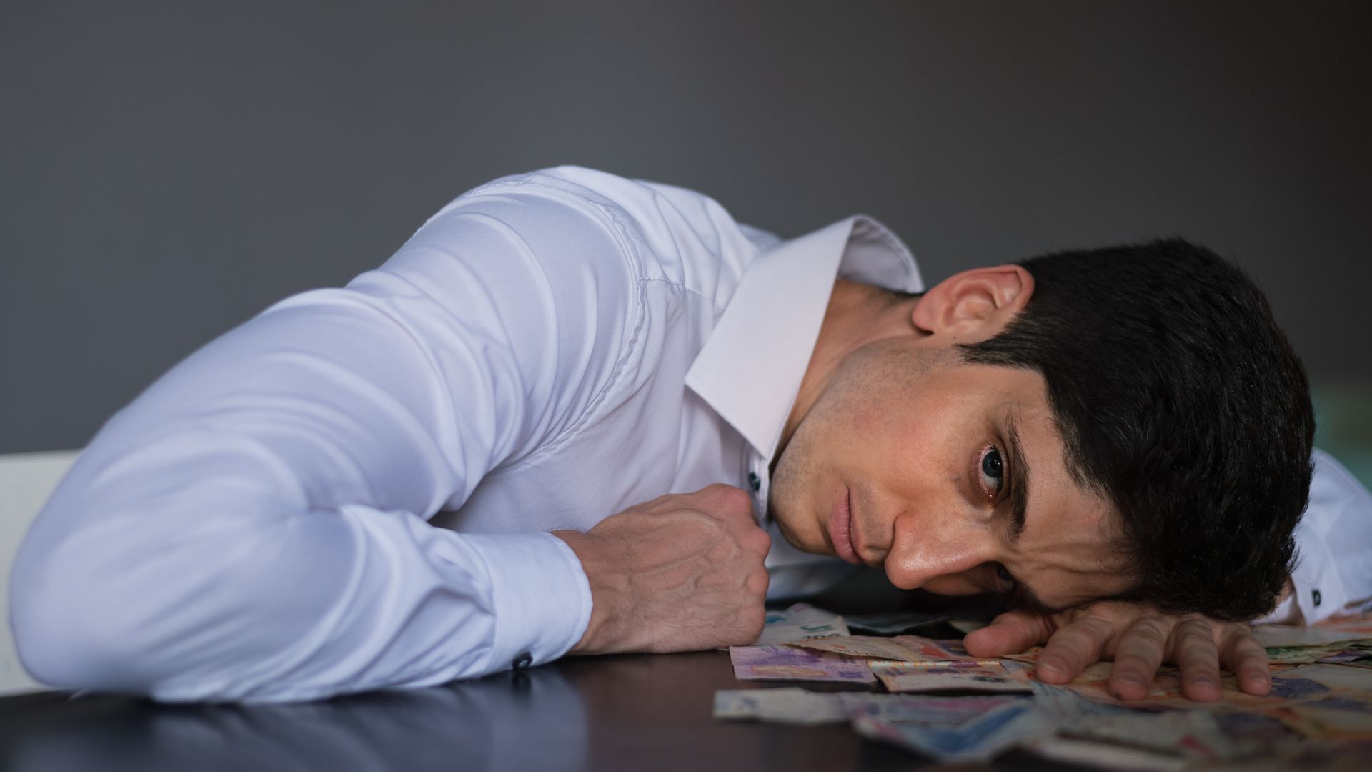 Armodafinil for Depression: An In-Depth Exploration Adult man in shirt lying on table, surrounded by currency, looking stressed indoors — armodafinil for depression