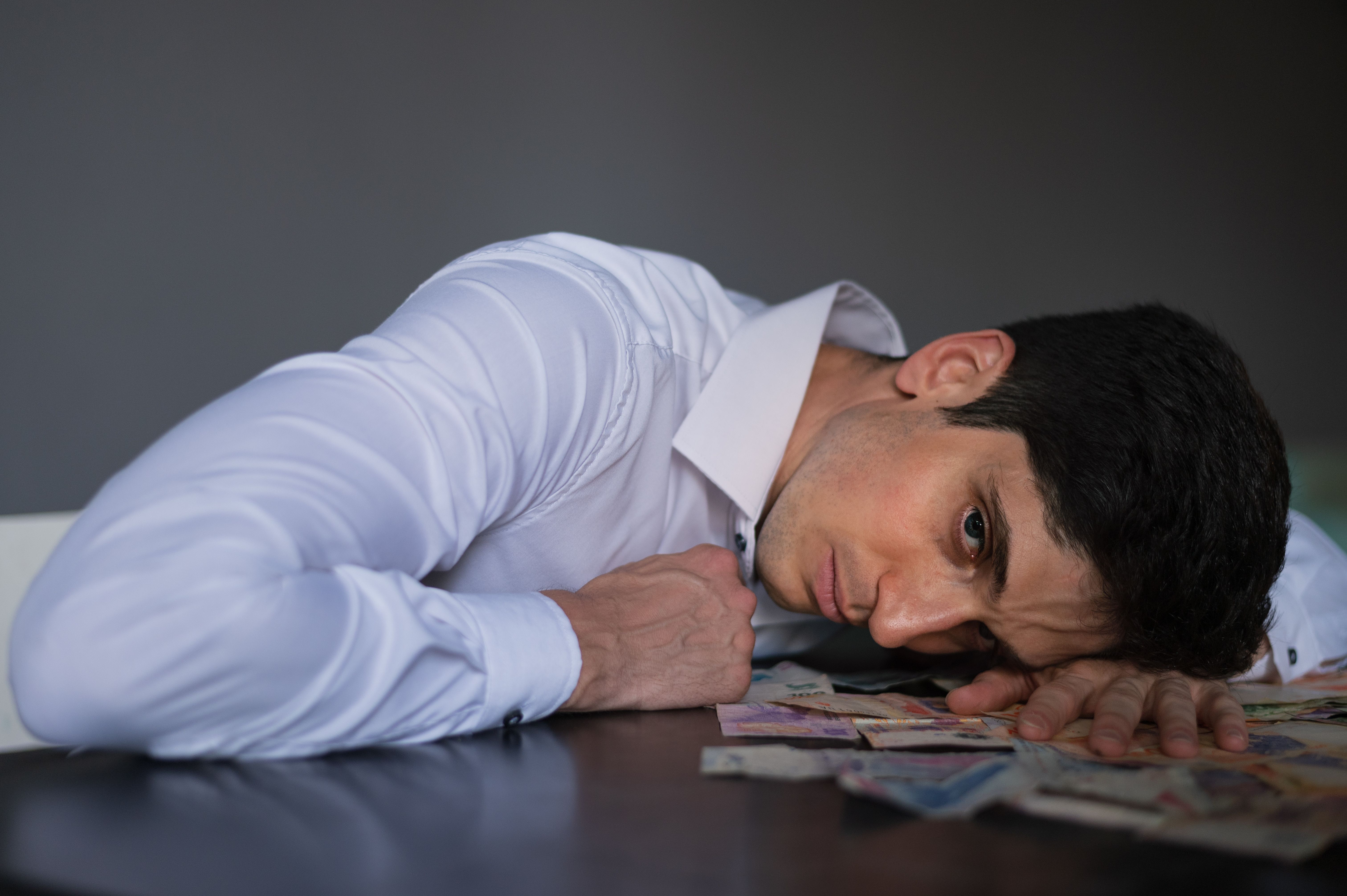 Gratis Hombre adulto con camisa acostado sobre una mesa, rodeado de dinero, con aspecto estresado en el interior. Foto de stock
