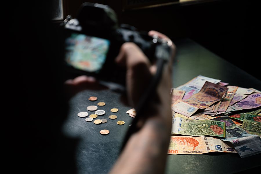 Close-up of Argentine peso notes and coins being photographed indoors.