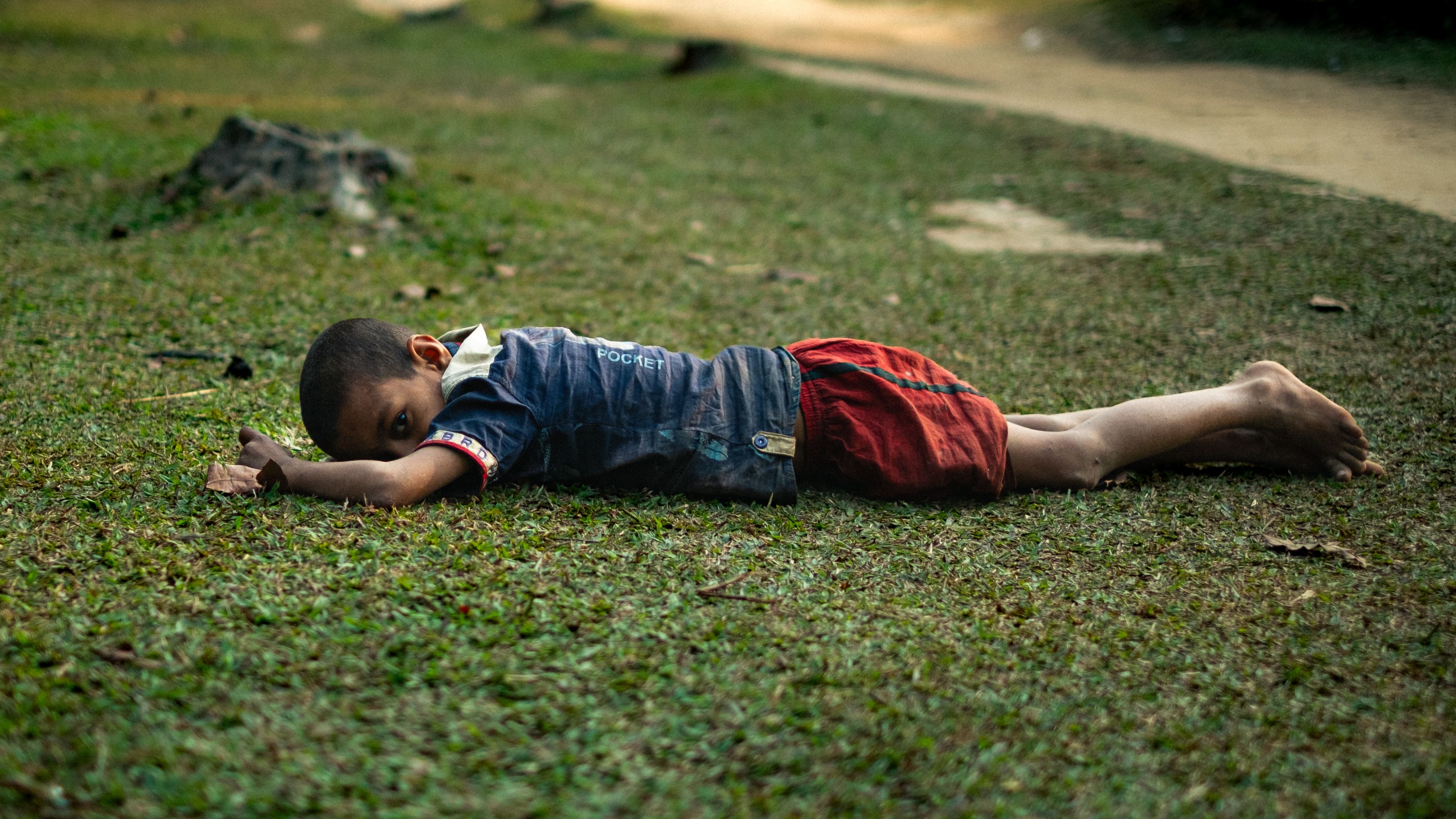 A young child lies peacefully on the grass in a serene outdoor setting.