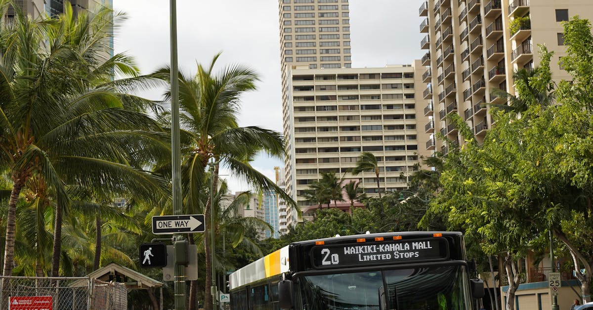 Photo by Aleksandr Poklad Bustling street in Honolulu featuring a city bus, pedestrians, and tall buildings under a cloudy sky.