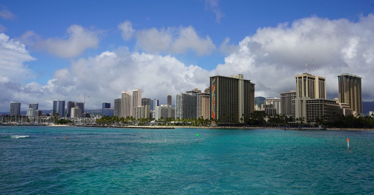 Photo by Aleksandr Poklad Vibrant view of Honolulu's skyline across turquoise waters with a cloudy blue sky.