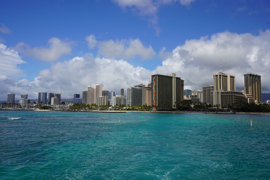 Photo by Aleksandr Poklad Vibrant view of Honolulu's skyline across turquoise waters with a cloudy blue sky.