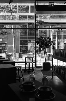 Black and white image of a modern cafe in Berlin, featuring seating, plants, and street view.
