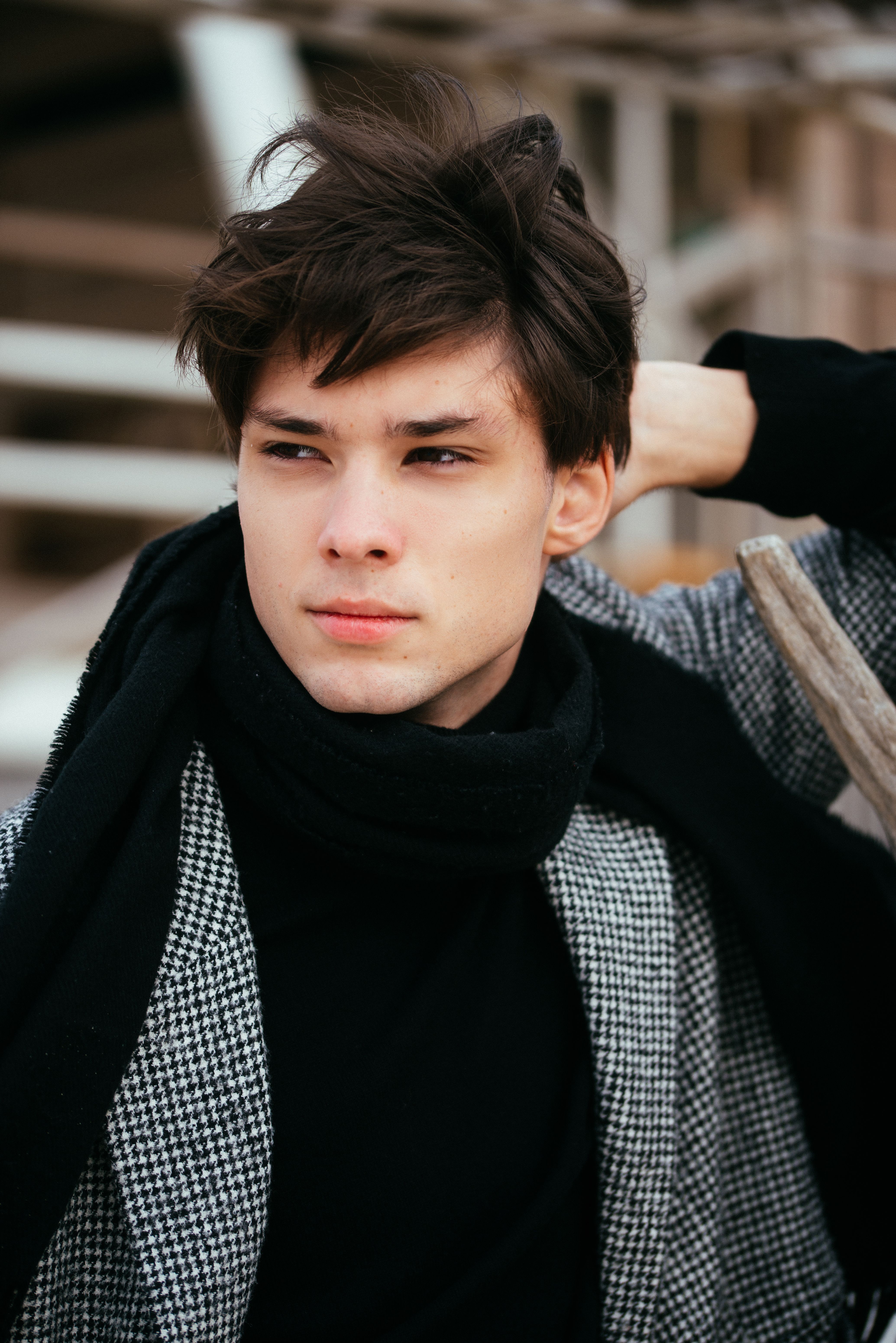 Portrait of a fashionable young adult male wearing a scarf and coat in an outdoor setting.