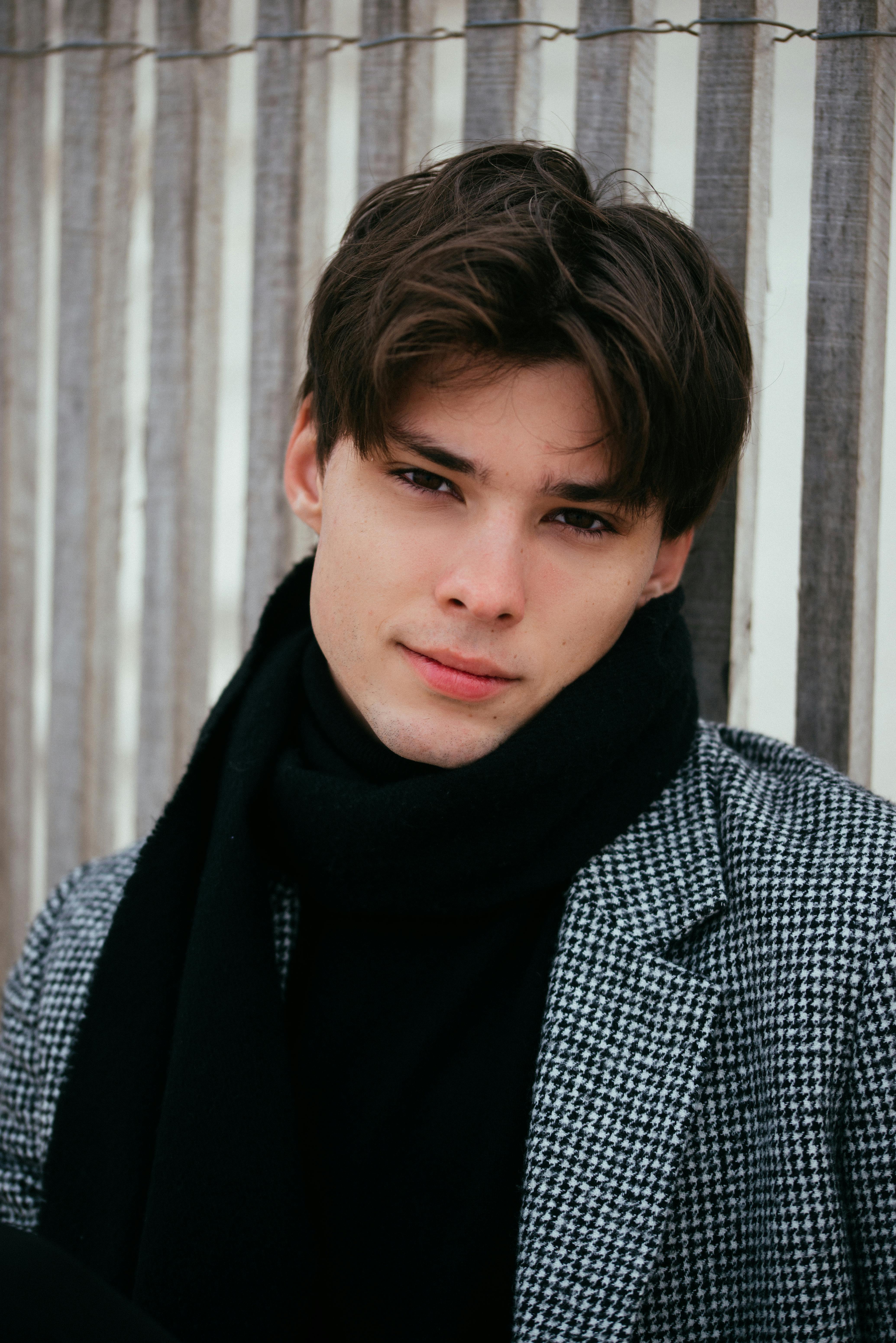 Portrait of a fashionable young man in a checkered coat and scarf against a wooden backdrop.