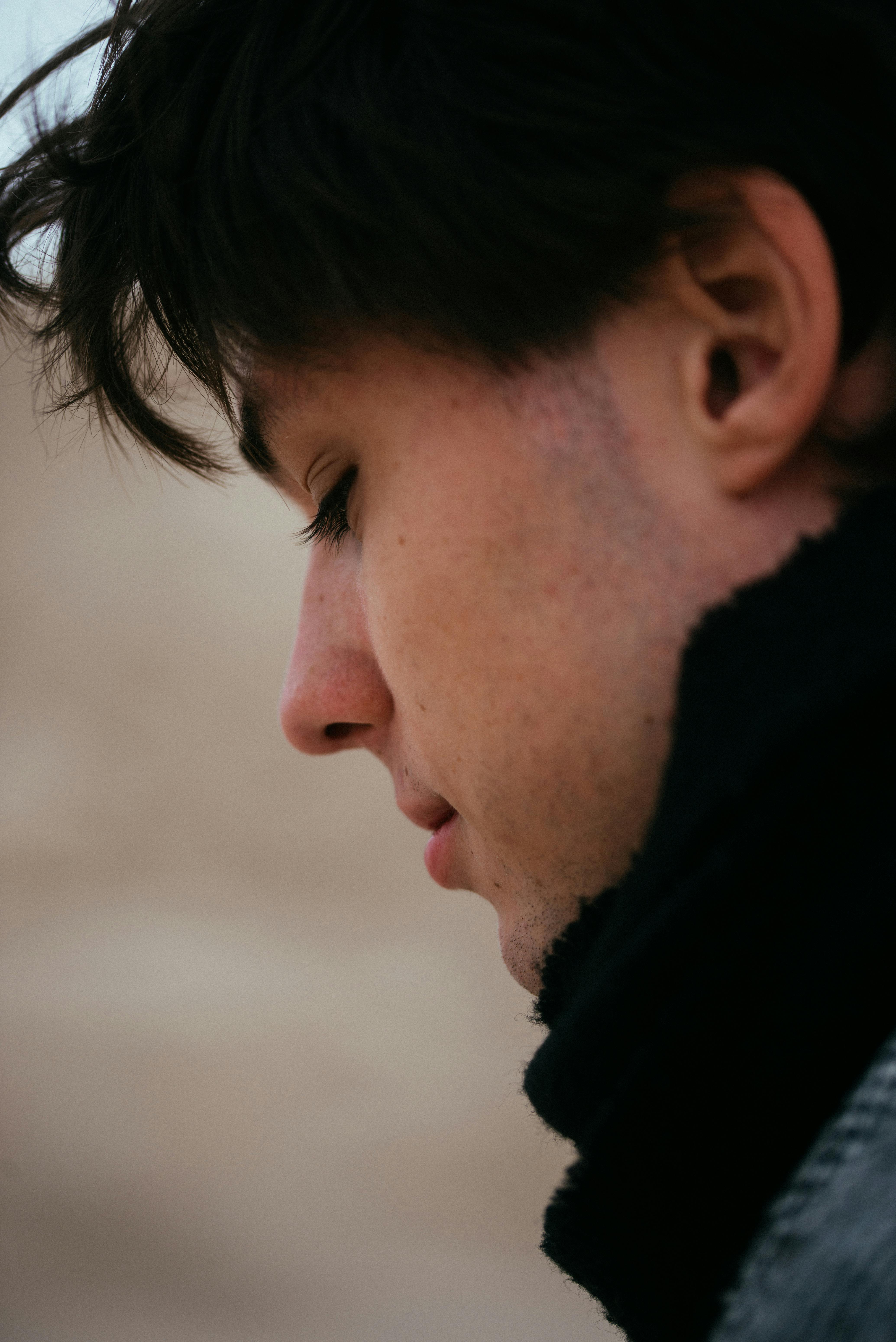 Close-up side profile of a young man in winter clothing outdoors, contemplating something.