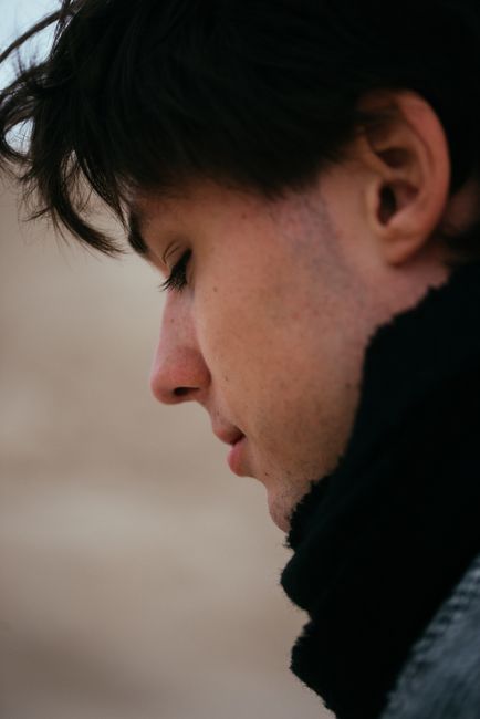 Close-up side profile of a young man in winter clothing outdoors, contemplating something.