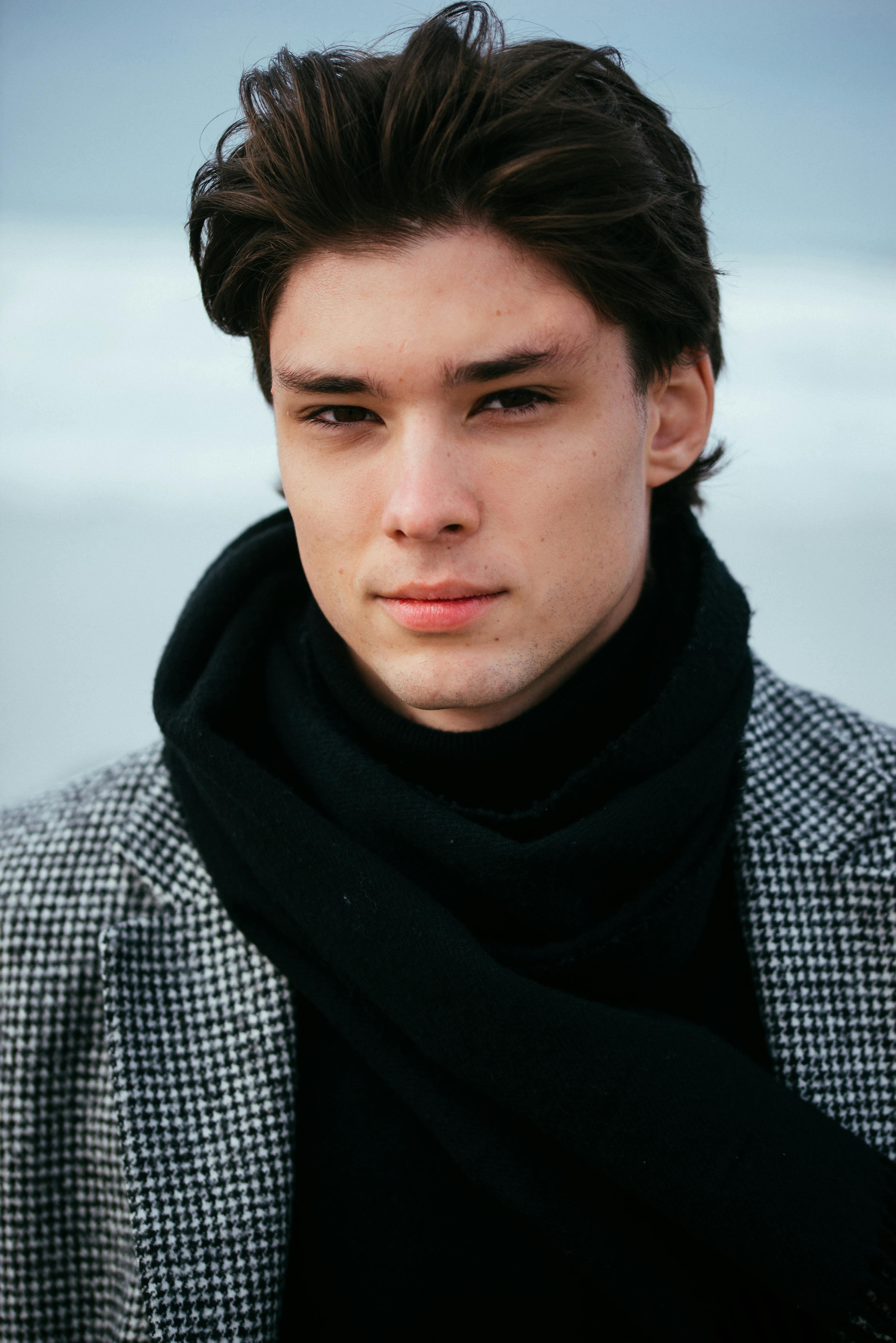 Portrait of a young man wearing a winter coat and scarf at the beach on a cold day.