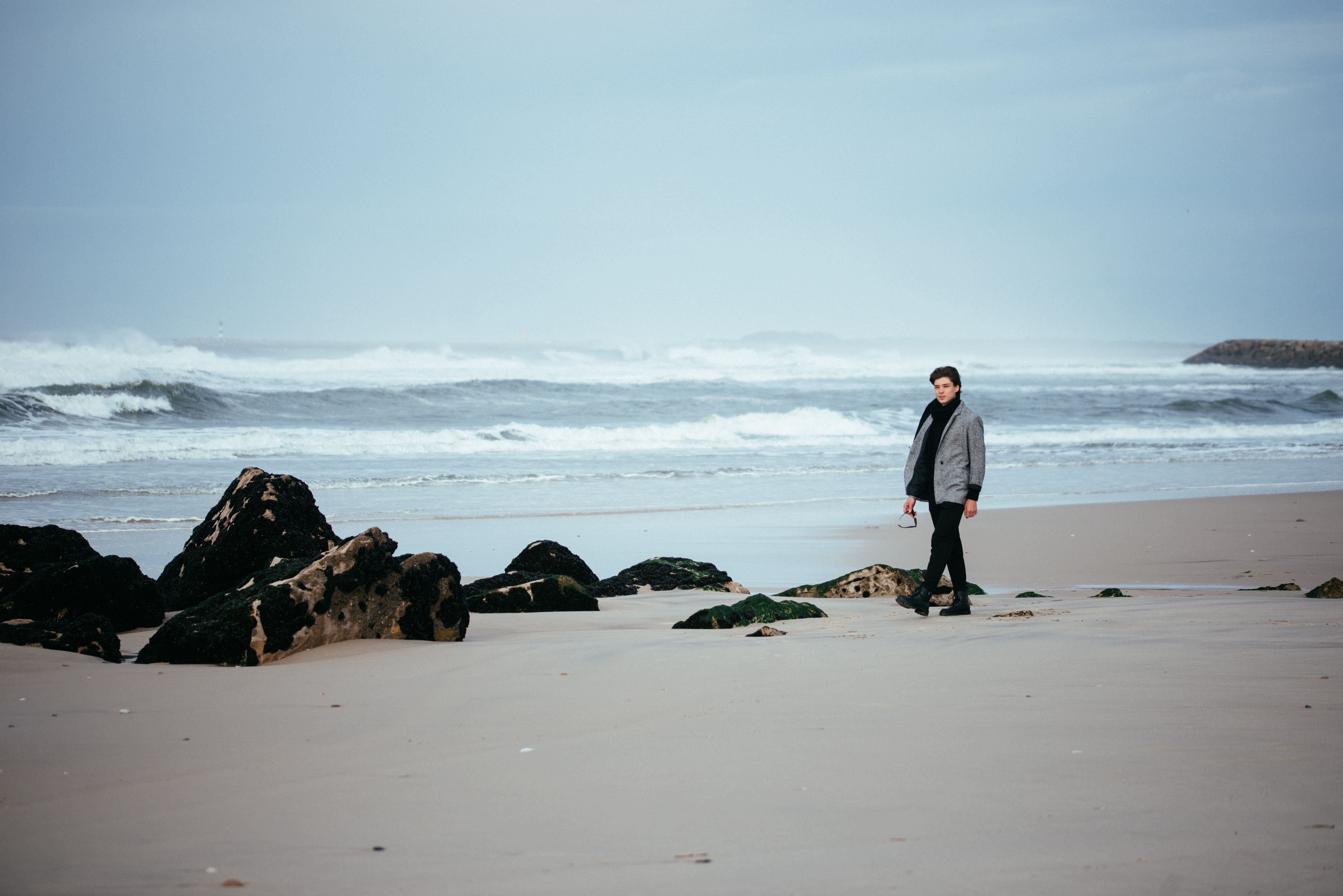 A lone person walking along a scenic beach with rocks and waves.