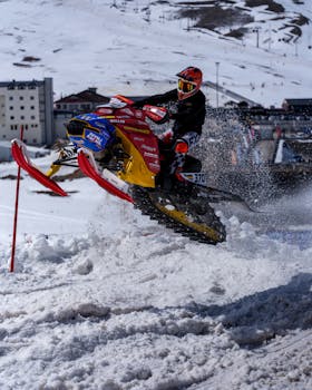 Exciting snowmobile race through snowy alpine landscape, showcasing winter sports action.
