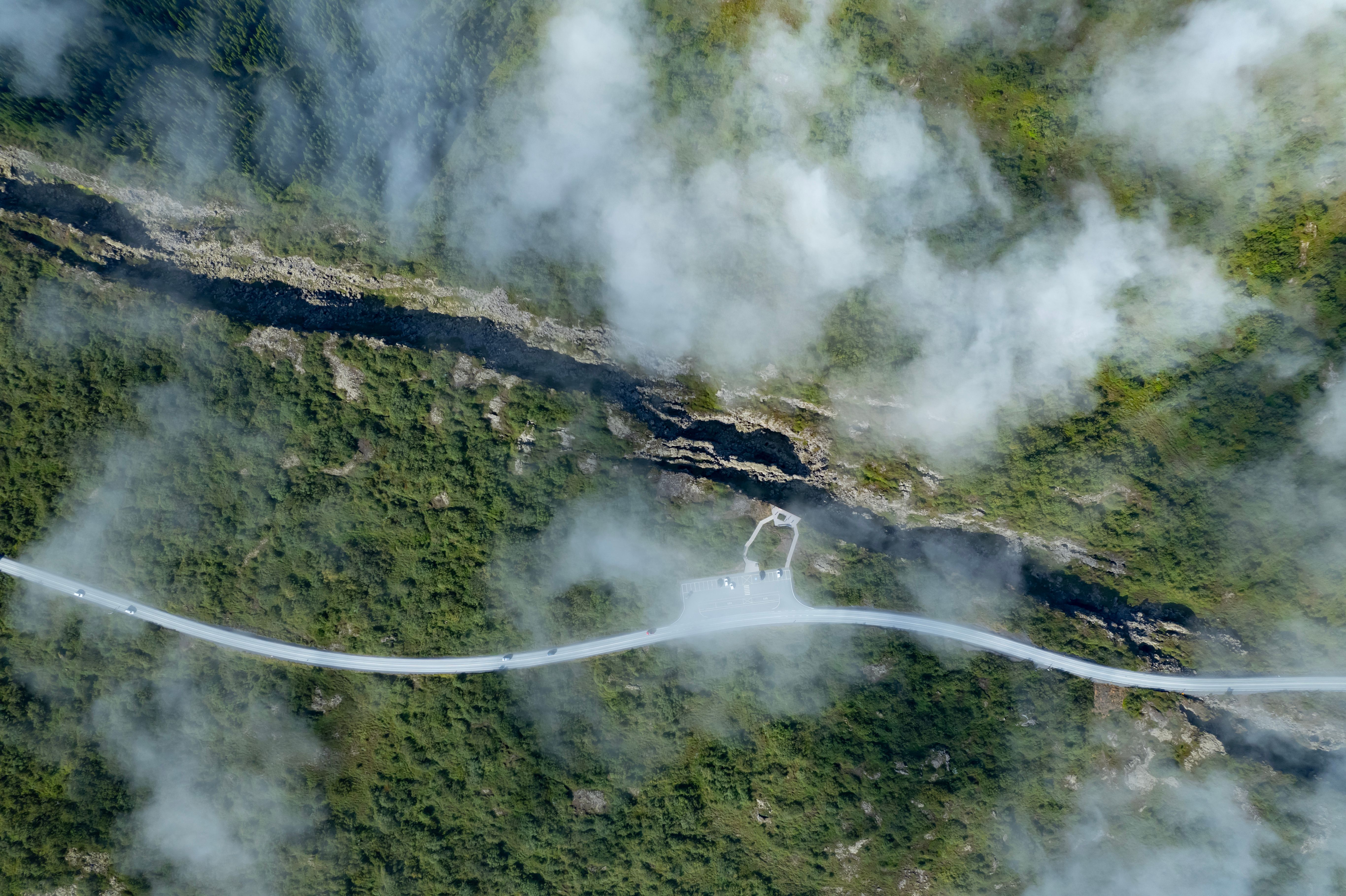 A breathtaking aerial view of a scenic road and geological rift amidst lush green landscape and clouds in Selfoss, Iceland.