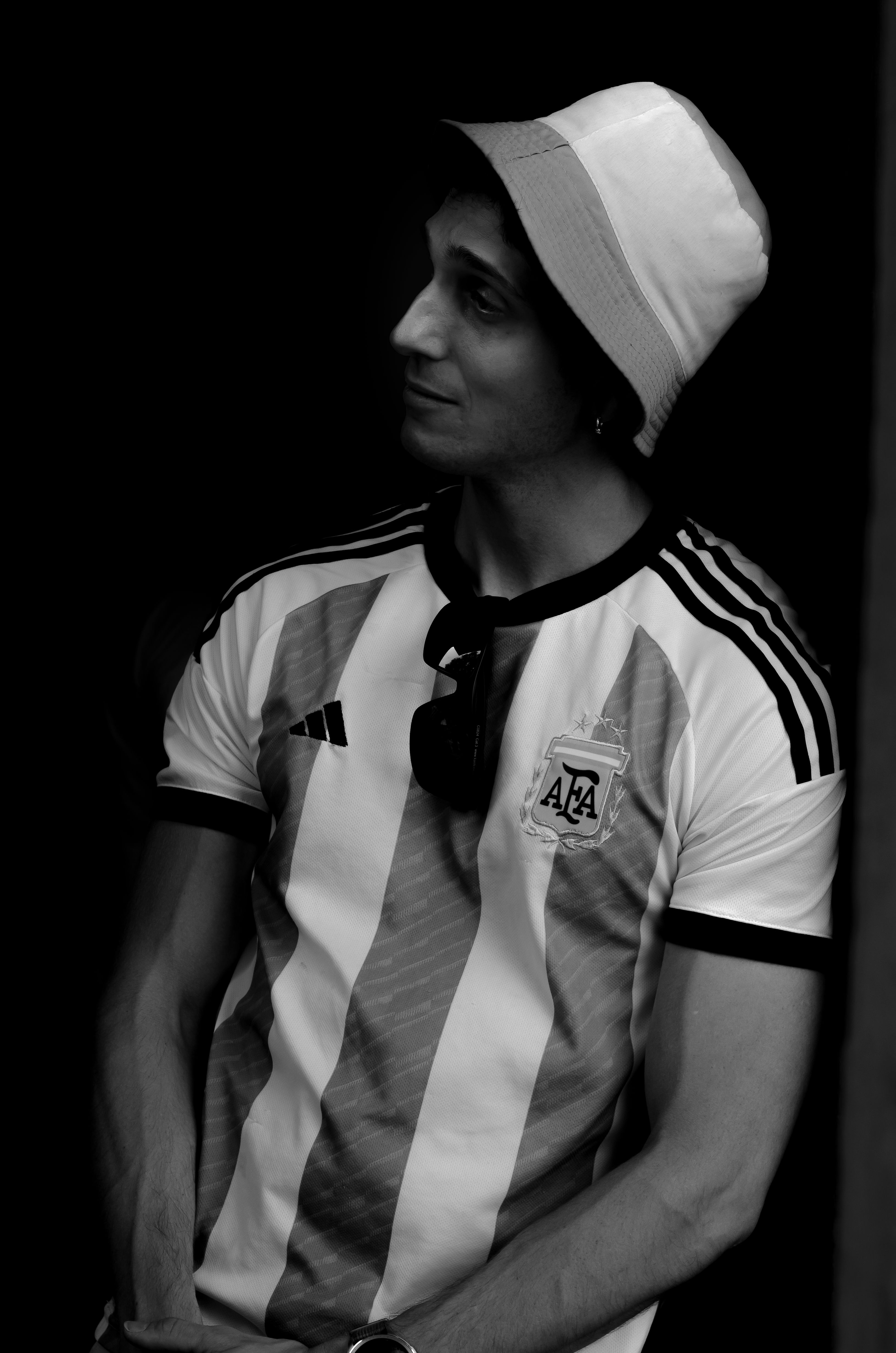 A stylish man in an Argentina football jersey and hat in black and white.