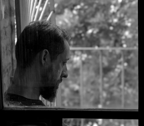 Free A contemplative male portrait captured in black and white through a window in Buenos Aires. Stock Photo