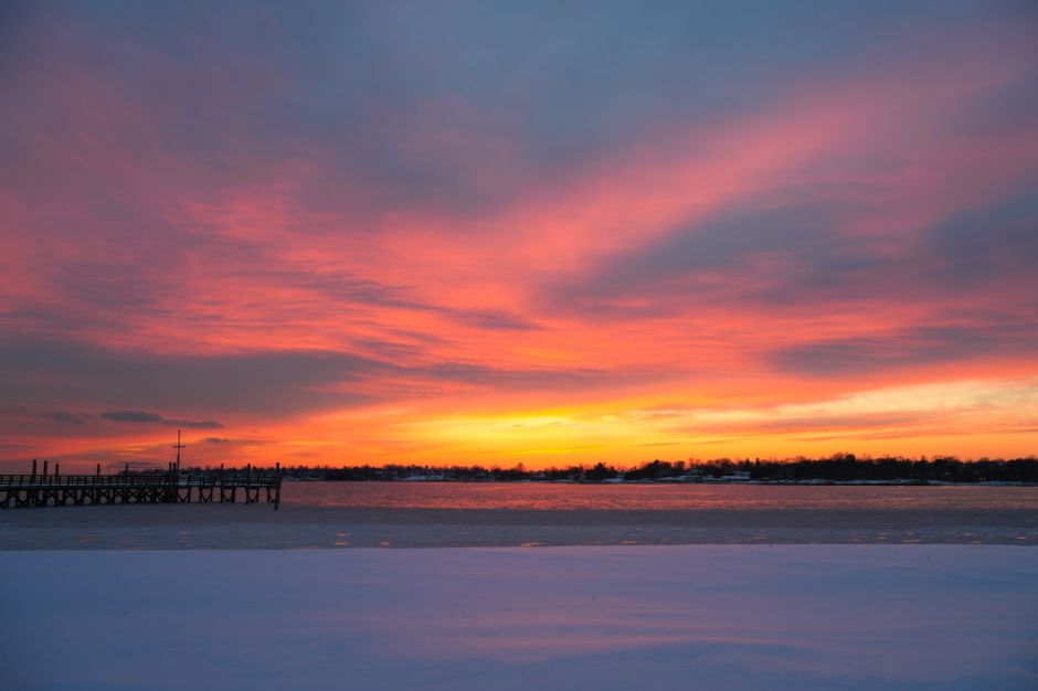 Stunning sunset with vivid colors over a snowy lakeside pier. Perfect winter landscape.