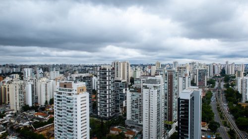 Free Aerial view of a bustling urban cityscape with tall skyscrapers and cloudy sky. Stock Photo