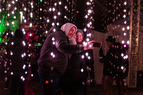 Free A couple takes a selfie among glowing festival lights, captured during a magical winter night. Stock Photo