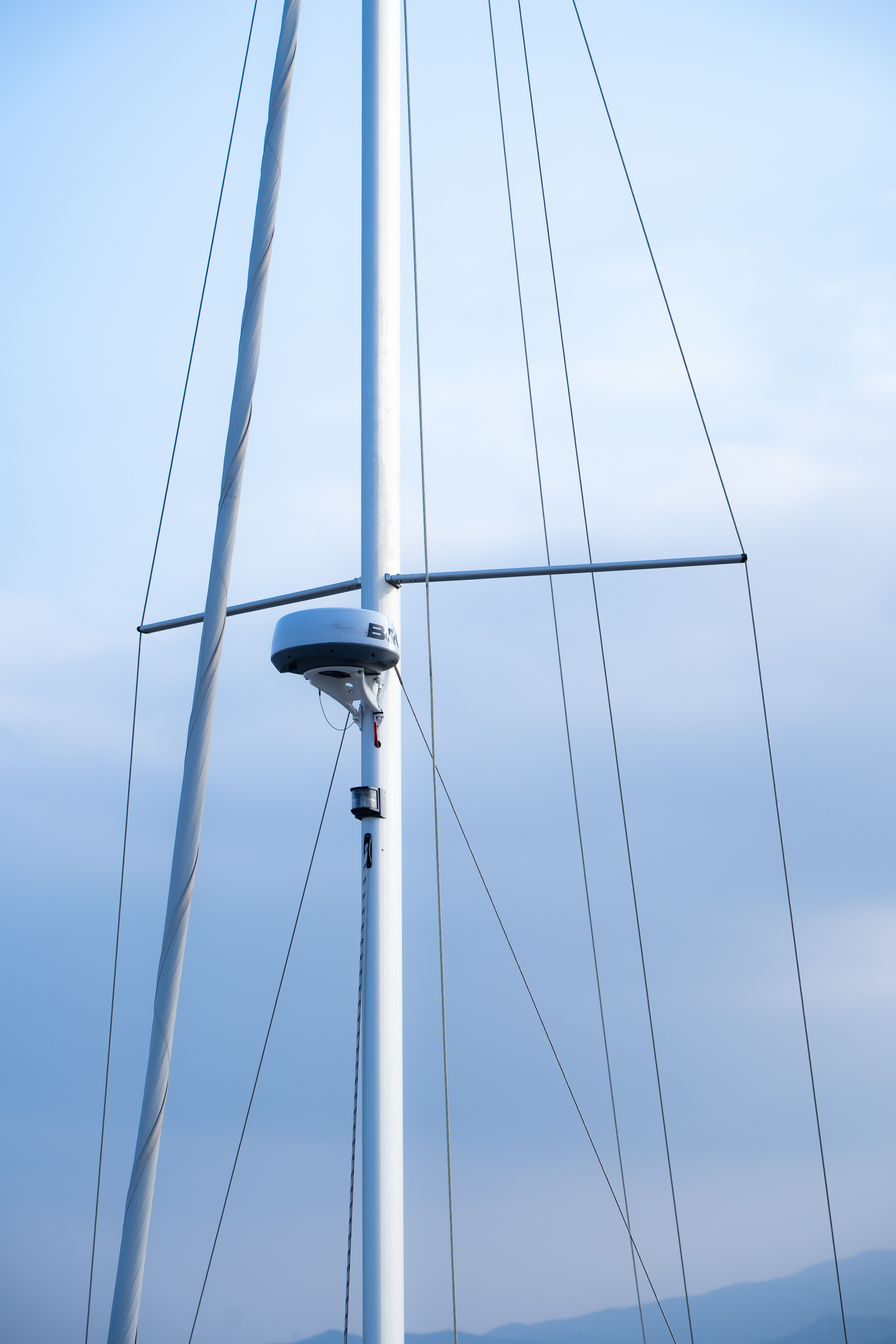 Sailboat mast with rigging lines against a serene blue sky, suggesting tranquility.