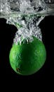 在黑色背景下，充满活力的绿酸橙在水中溅起水花