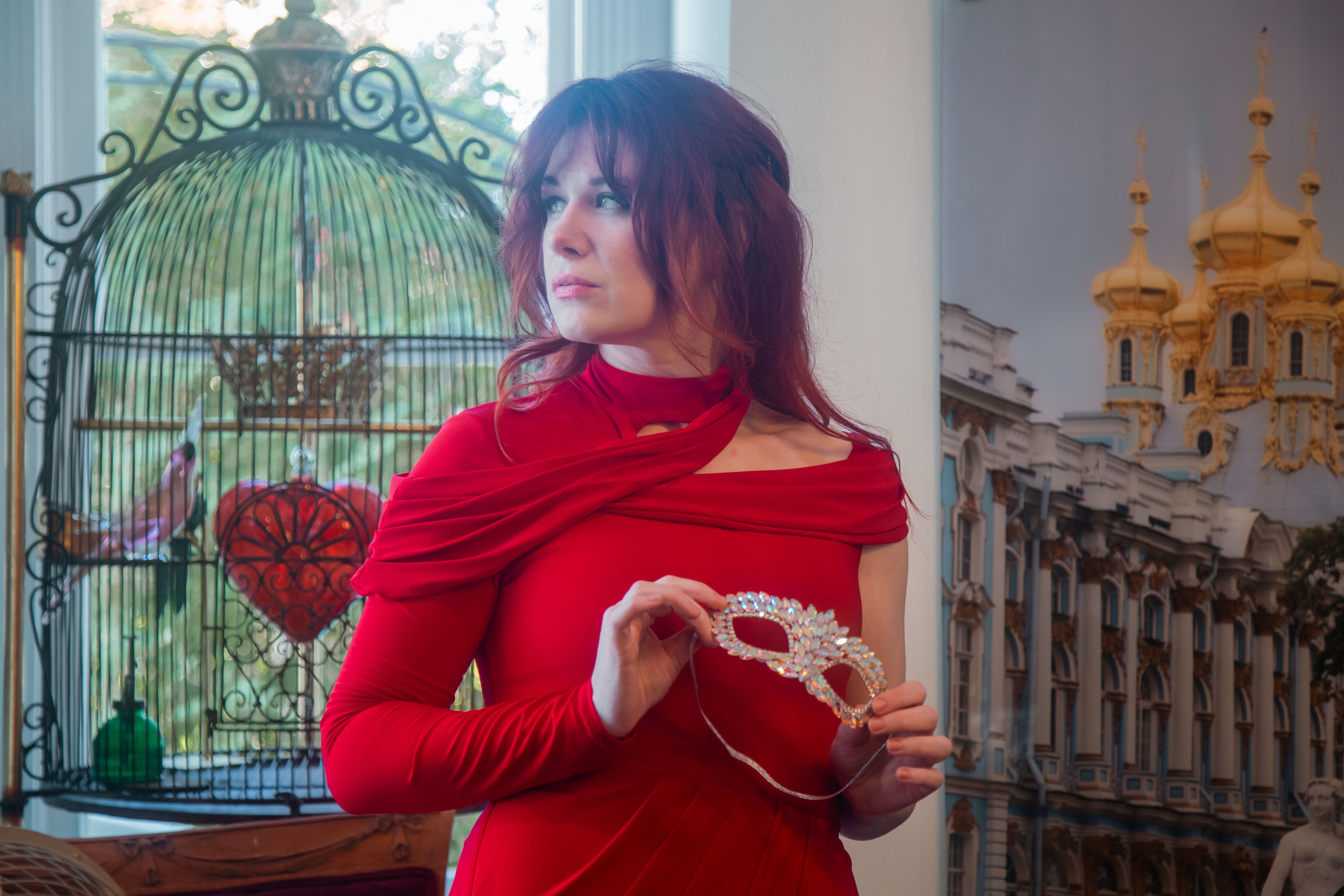 Stylish woman in red holding a mask in a royal-themed setting.